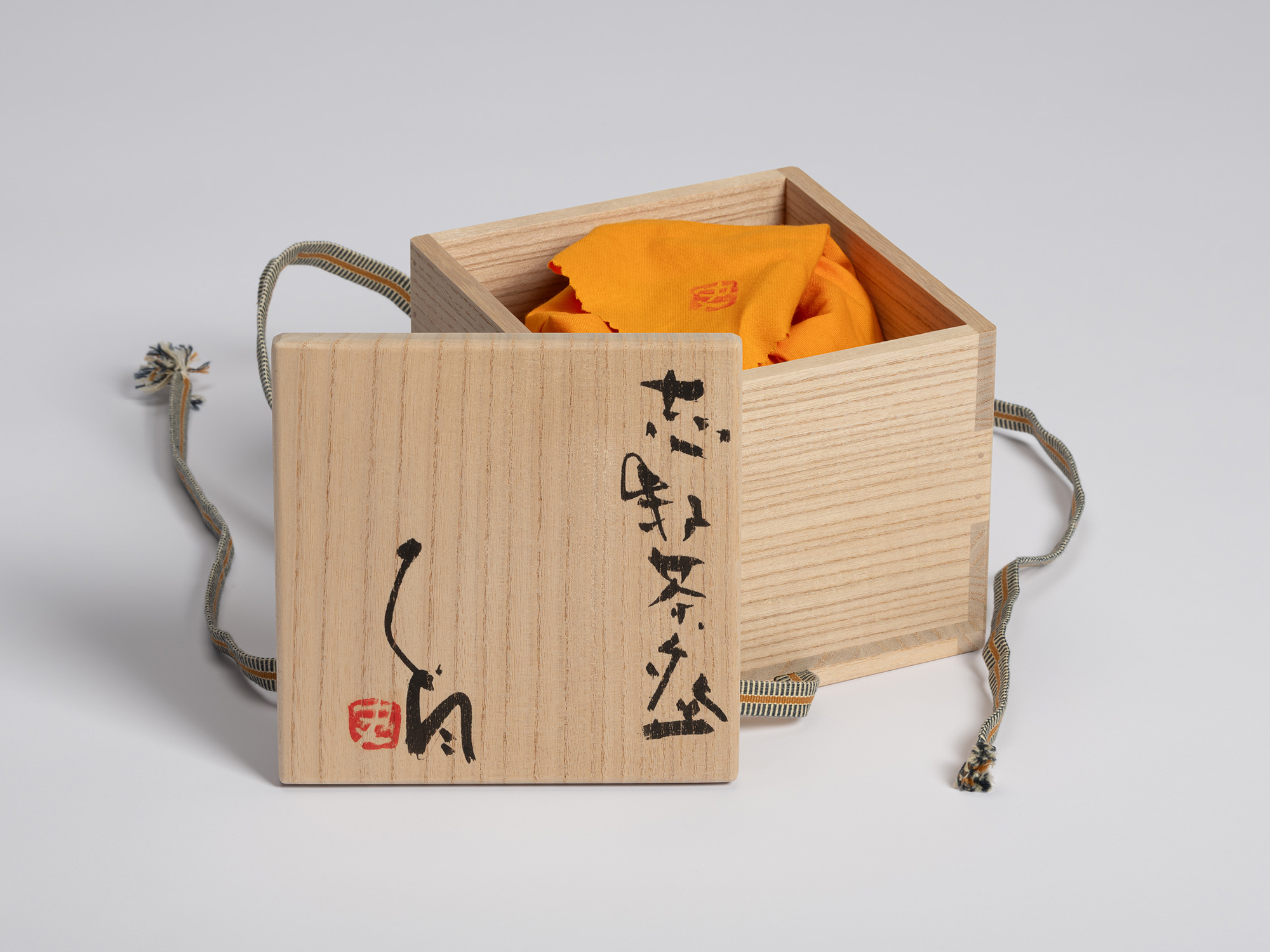 eamless light grey background. The square box is open, with its square lid propped vertically against...