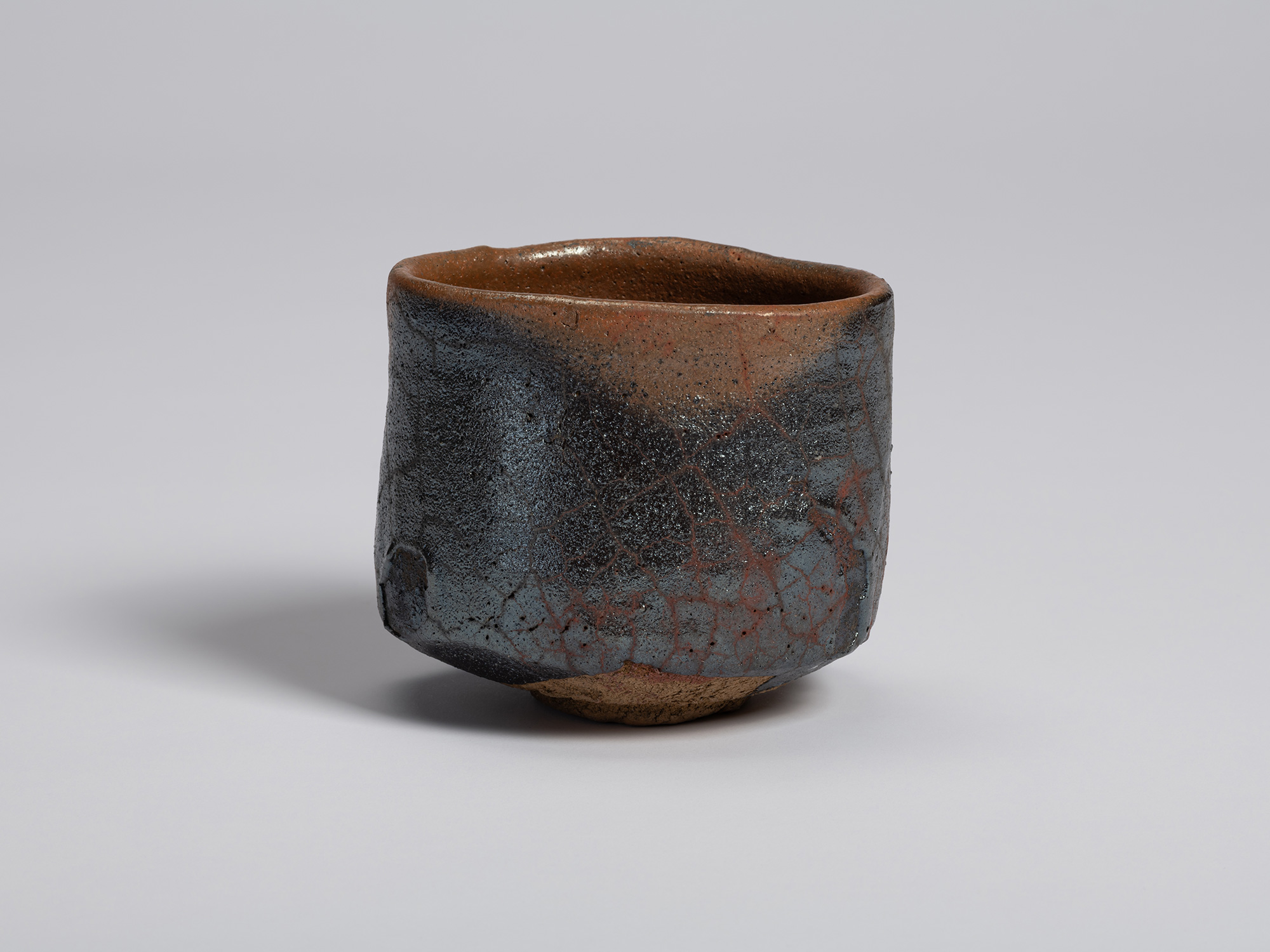 Front view of the tea bowl highlighting a vertical band of reddish-brown clay framed by darker...