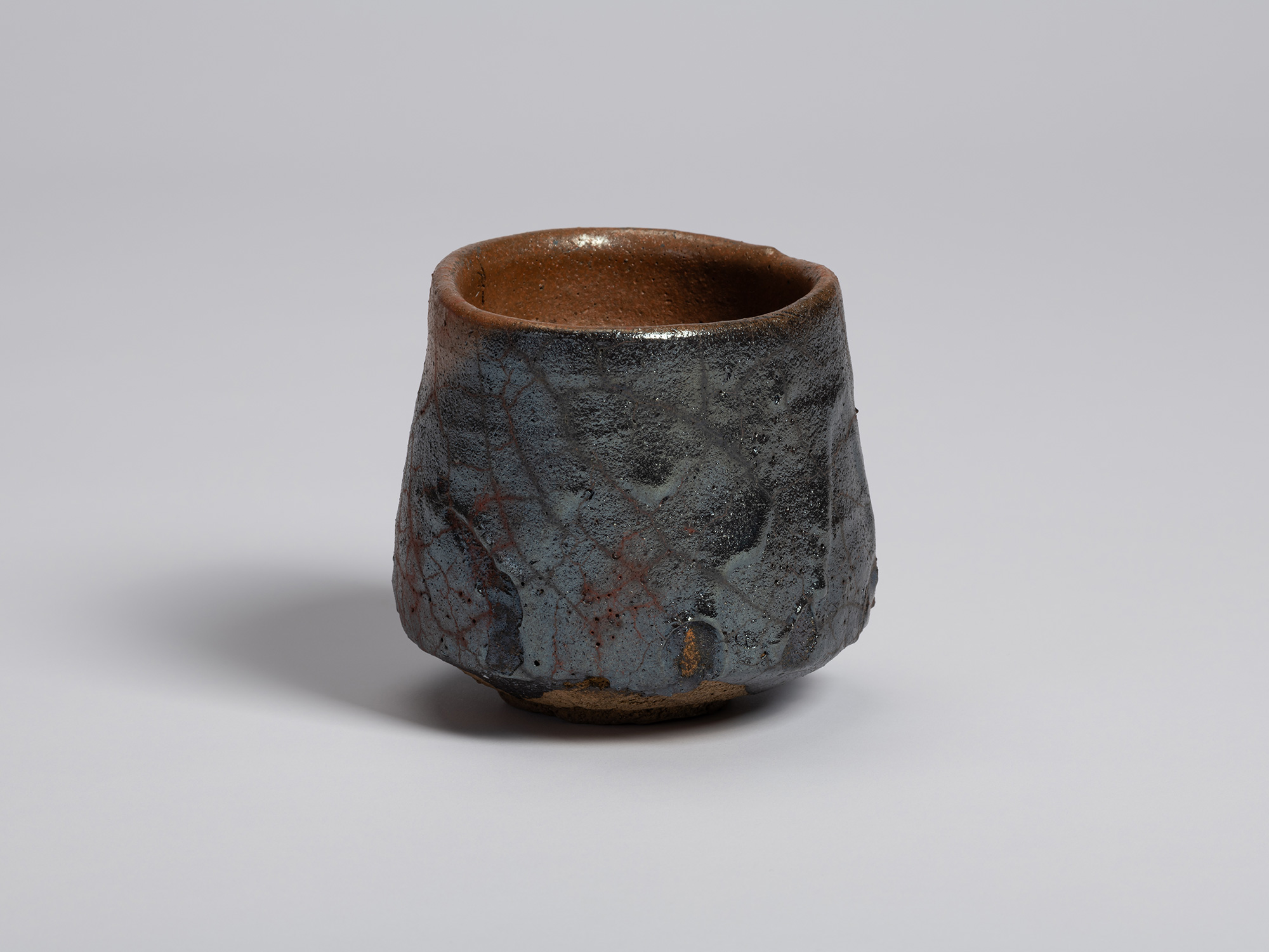 View of the tea bowl showing a predominantly dark, glossy surface with fine crackle lines and scattered...