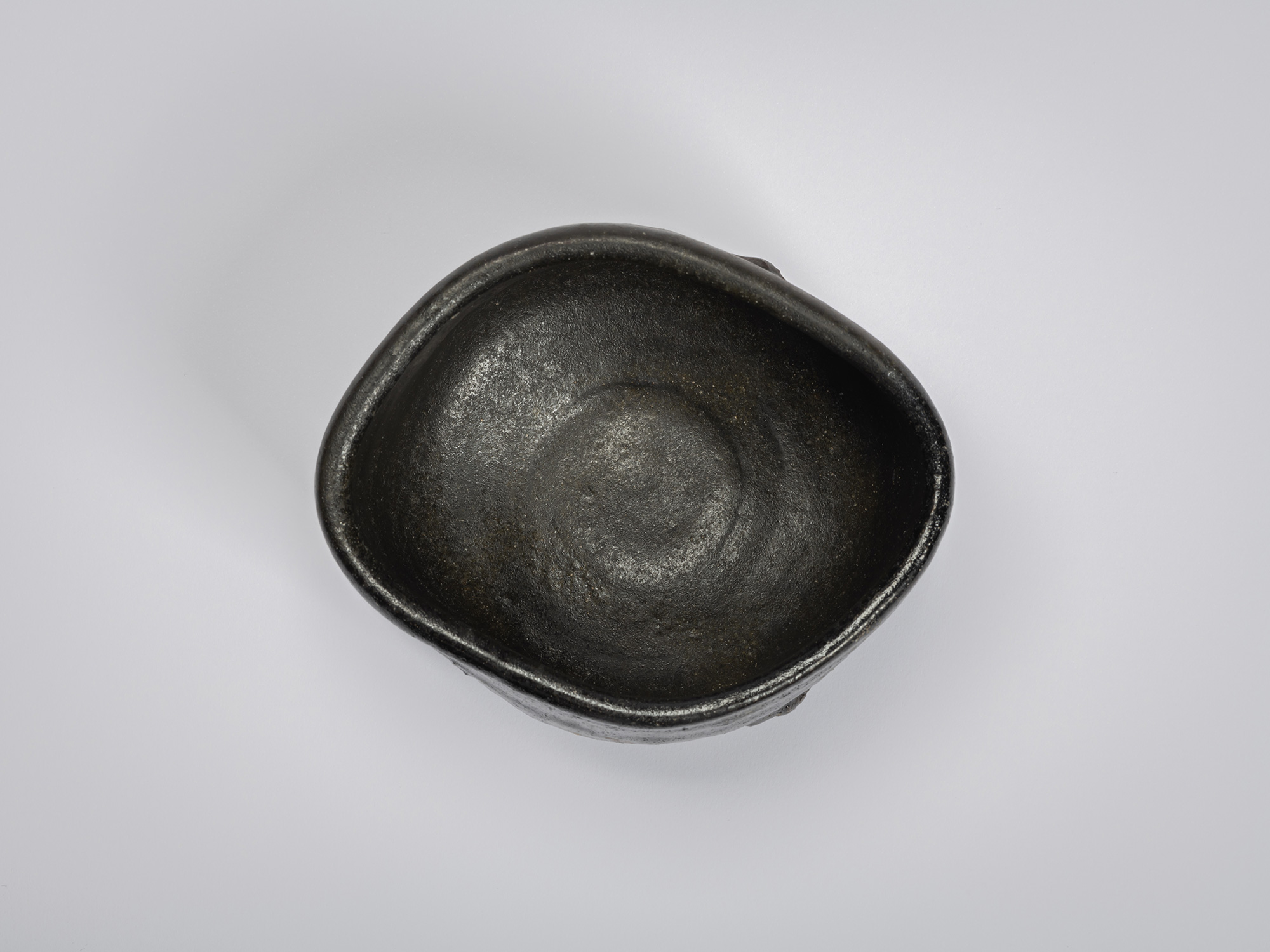 Overhead view of a hand-formed black tea bowl by Shiro Tsujimura. The interior is coated in a dark,...