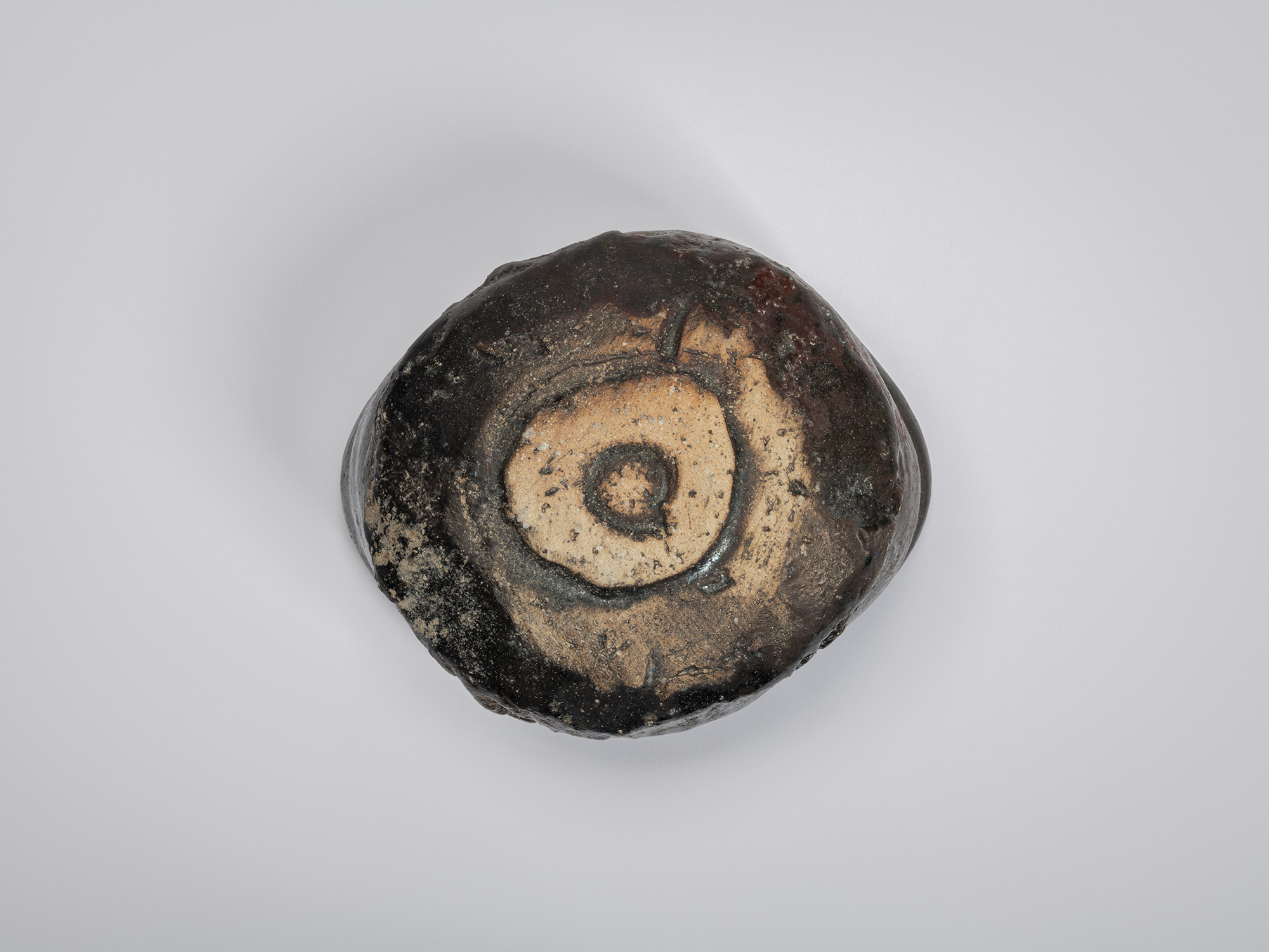 Bottom view of a black tea bowl by Shiro Tsujimura showing its irregularly shaped foot ring. The...