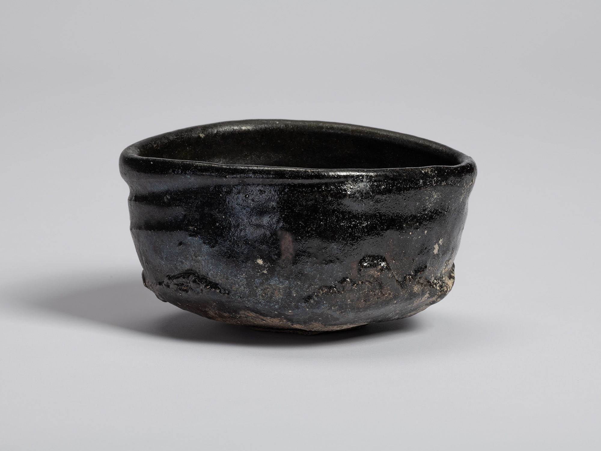 View of a hand-formed black tea bowl by Shiro Tsujimura. The bowl has an irregular, slightly compressed...
