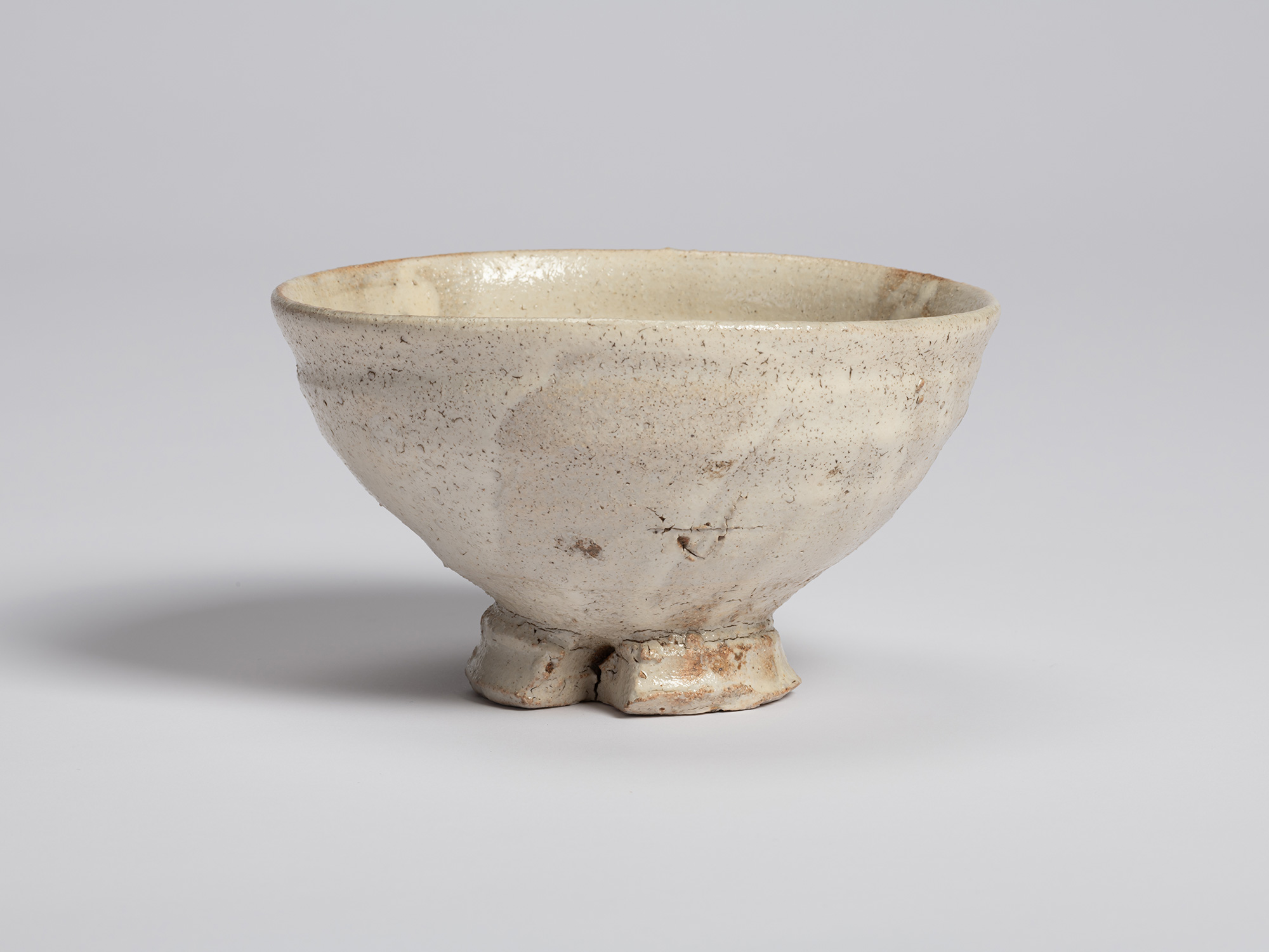 View of Shiro Tsujimura’s tea bowl with a tripodal foot. The white glazed surface reveals a slightly...