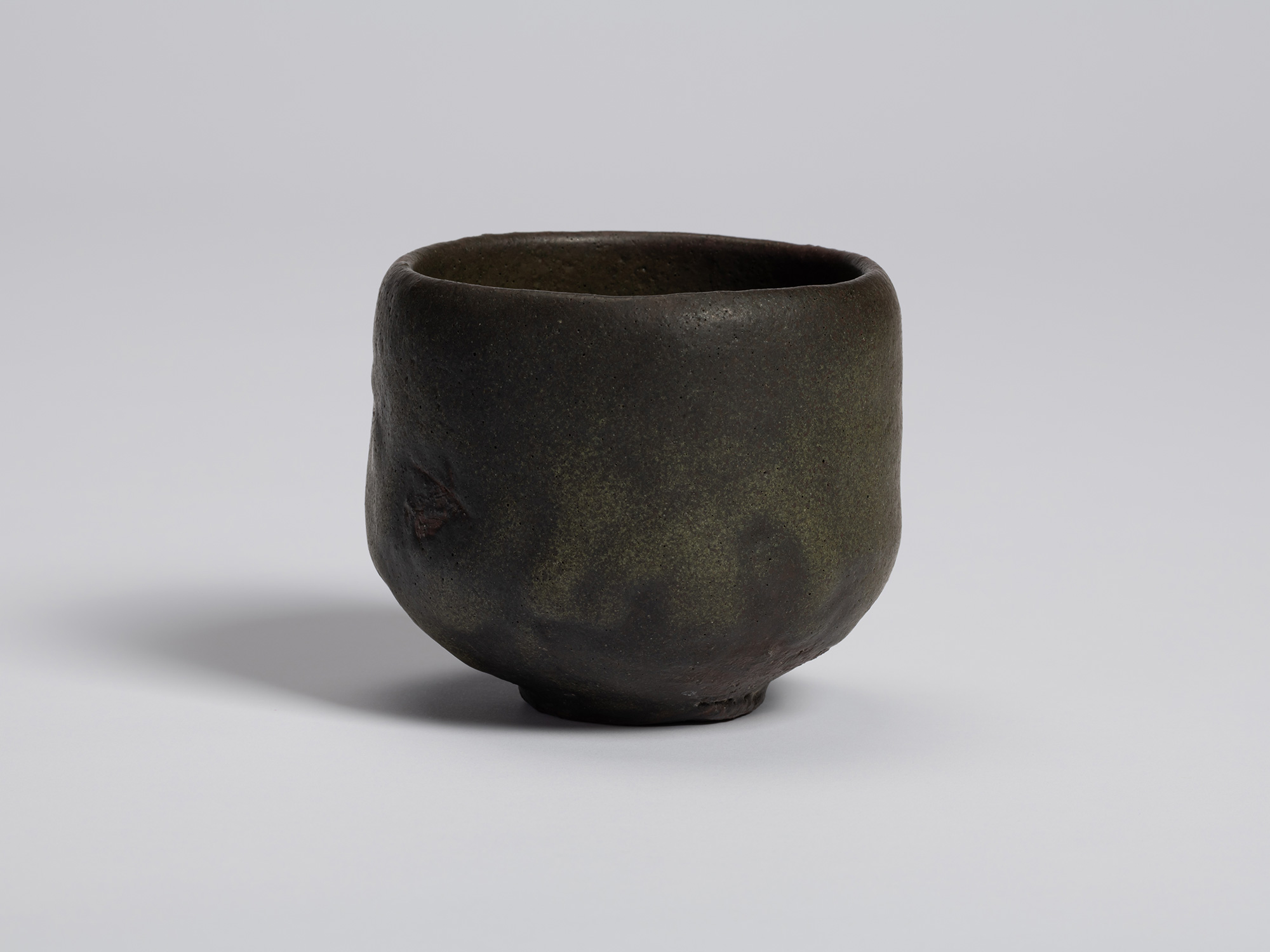 Front view of a kuro tea bowl by Shiro Tsujimura. The hand-formed bowl has gently rounded sides...