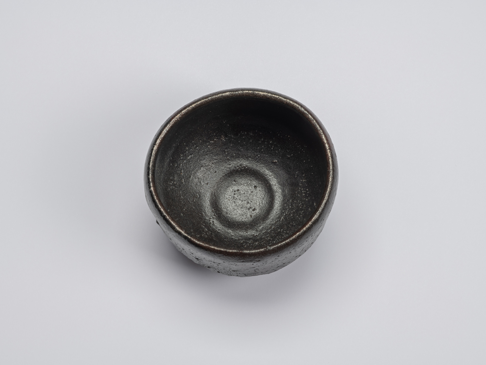 Overhead view of the black-glazed tea bowl showing a deep interior with a softly rounded well,...