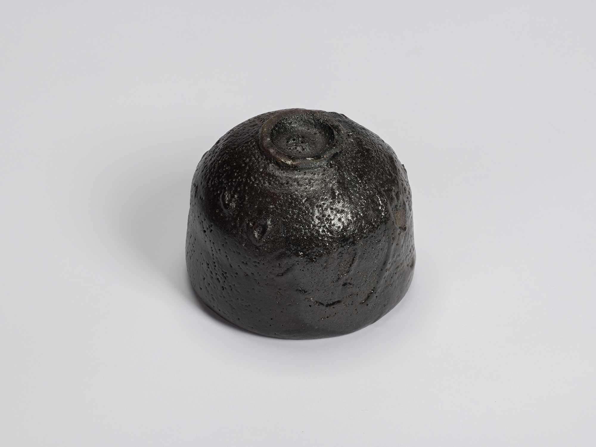 Underside of the black-glazed tea bowl showing a small circular foot ring surrounded by a rounded...