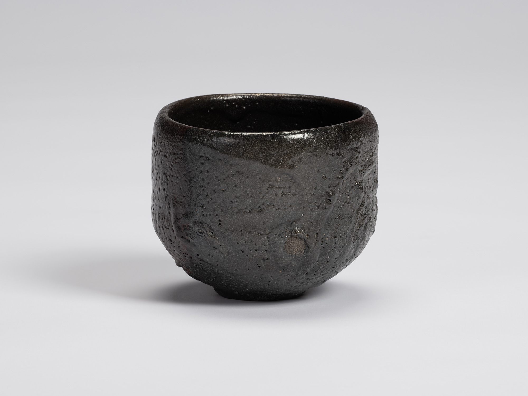 Black-glazed tea bowl by Shiro Tsujimura with a rounded cylindrical form, slightly tapered base,...
