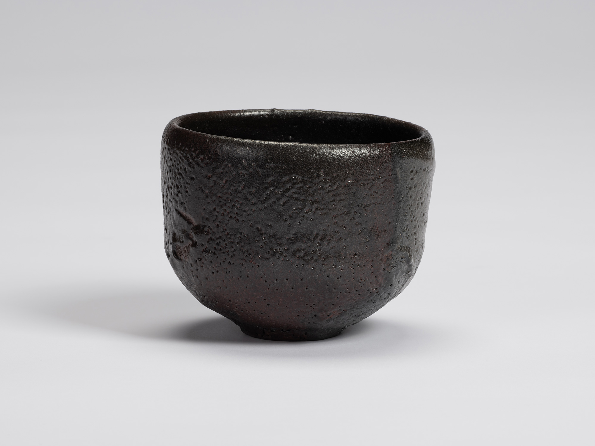 Black-glazed tea bowl by Shiro Tsujimura with a rounded cylindrical form, slightly tapered base,...