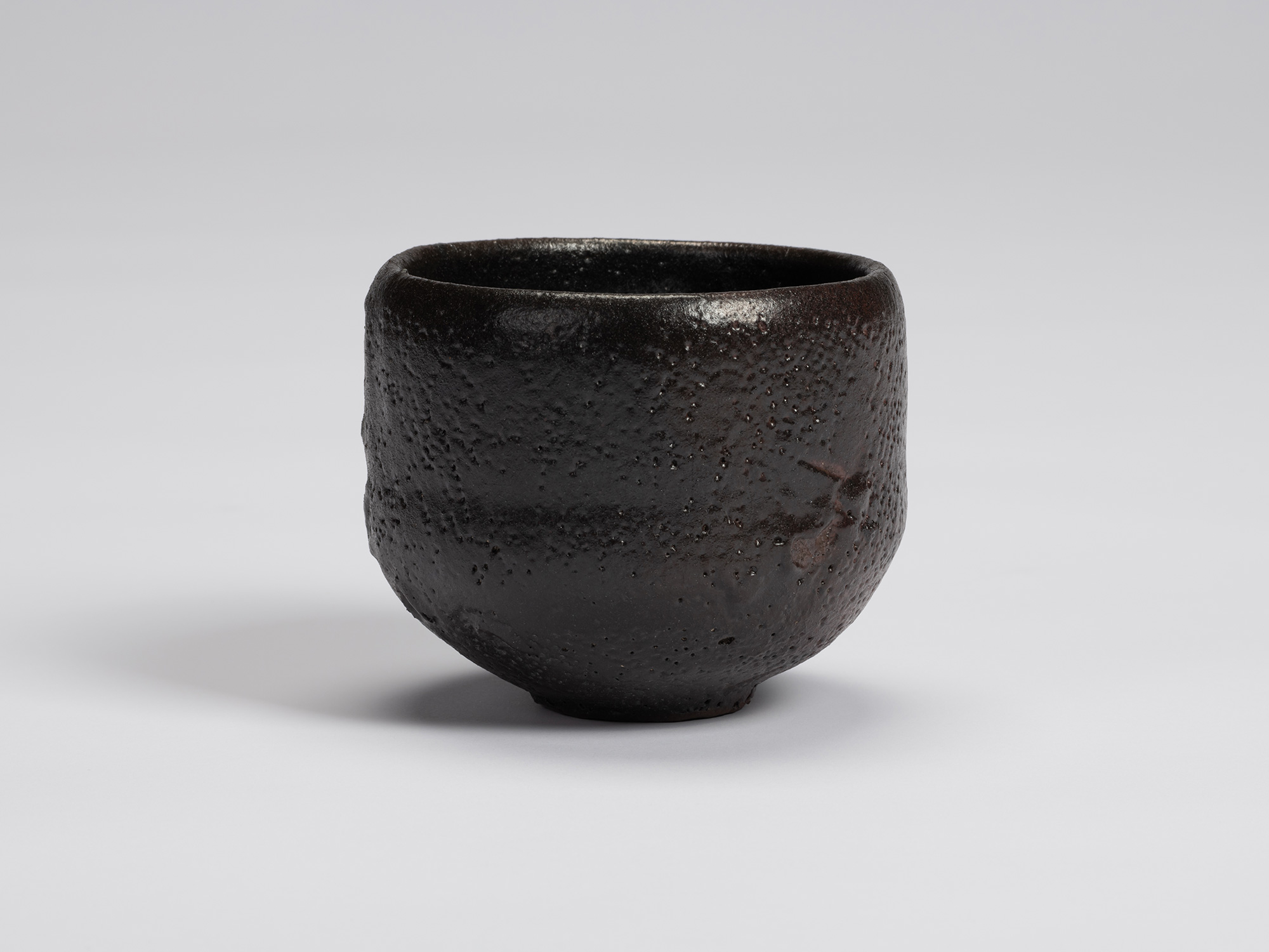 Black-glazed tea bowl by Shiro Tsujimura with a rounded cylindrical form, slightly tapered base,...