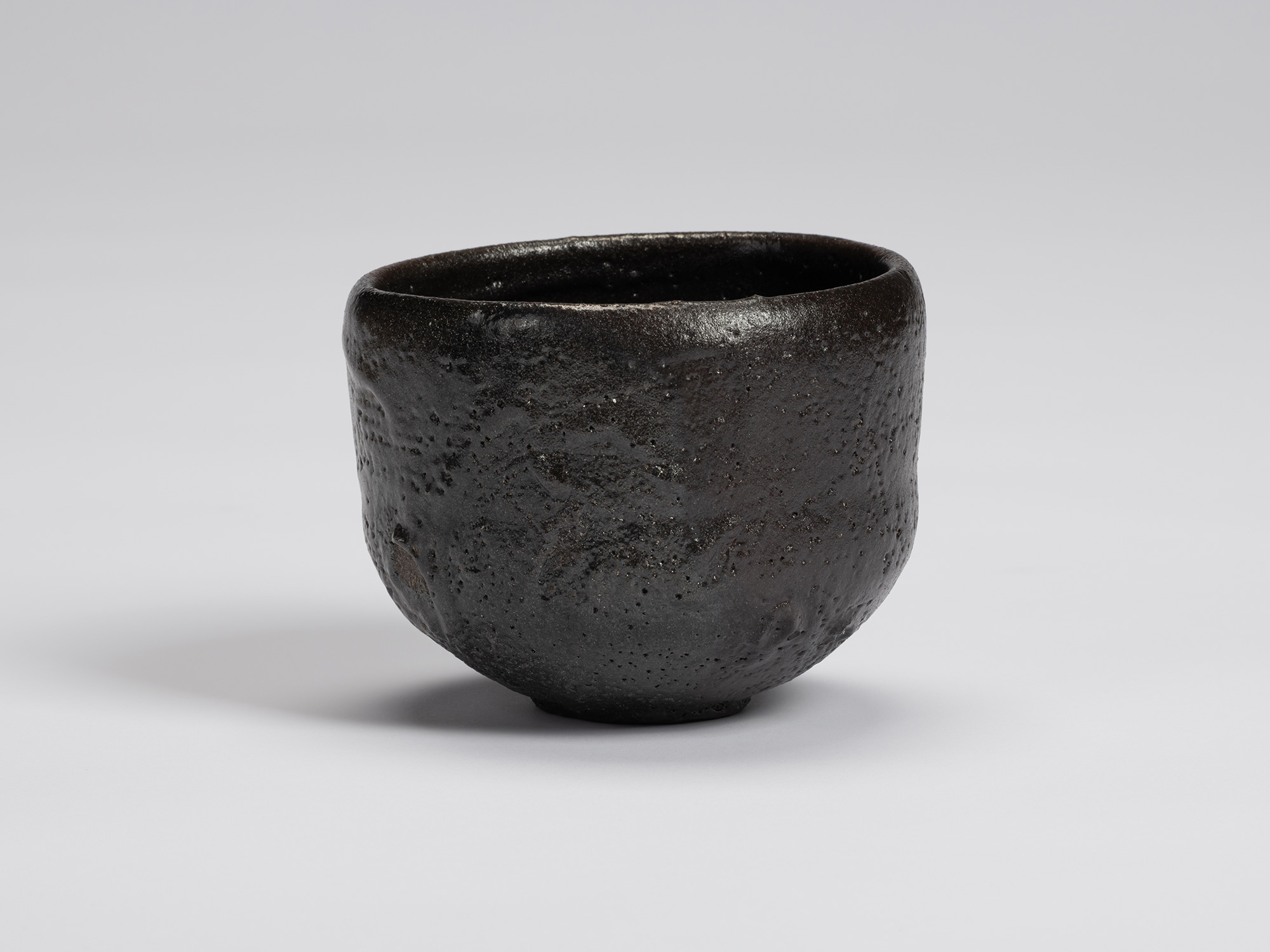 Black-glazed tea bowl by Shiro Tsujimura with a rounded cylindrical form, slightly tapered base,...