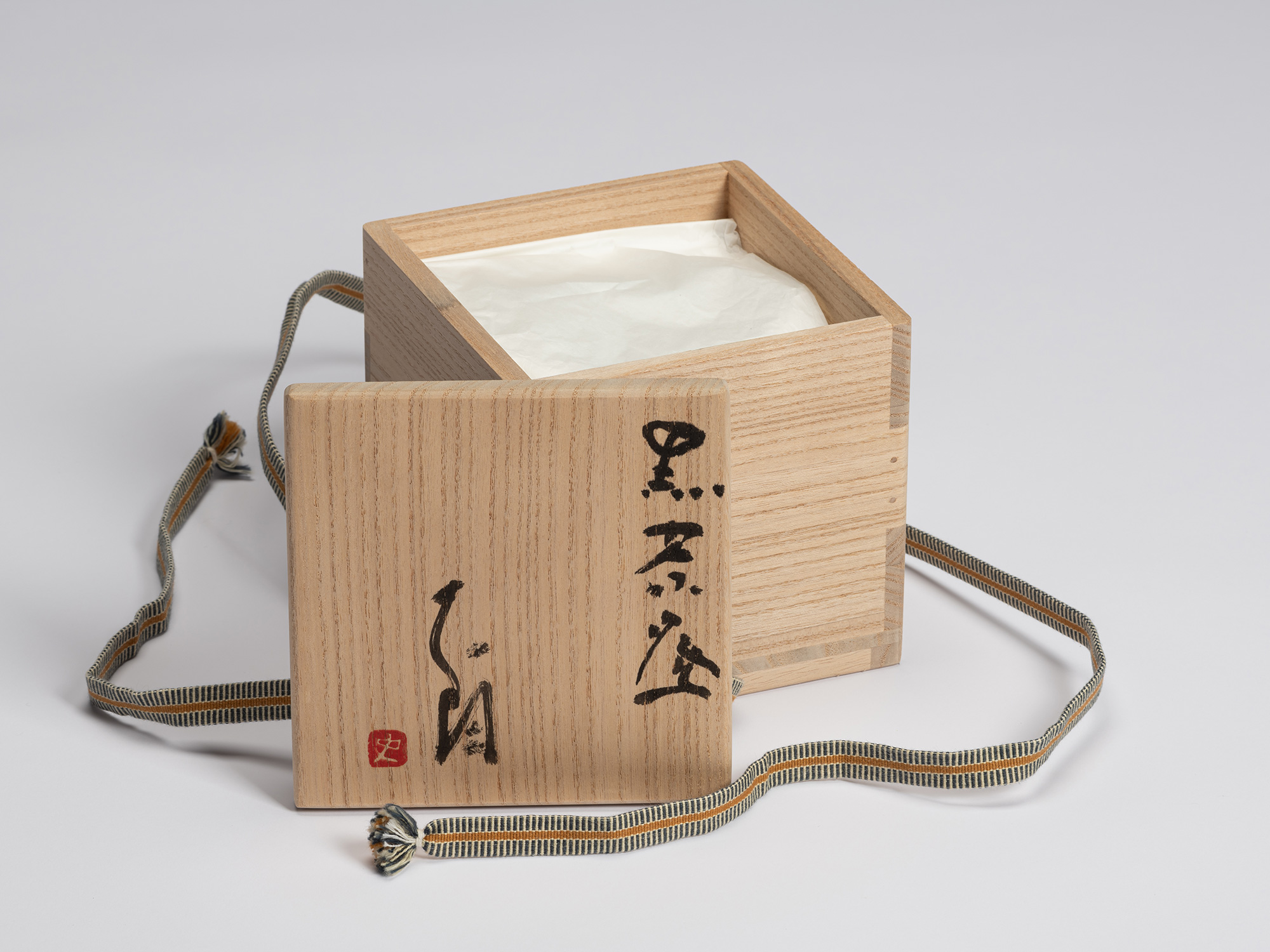 Open paulownia wood tomobako with the lid placed in front of the box. The lid is inscribed in black...