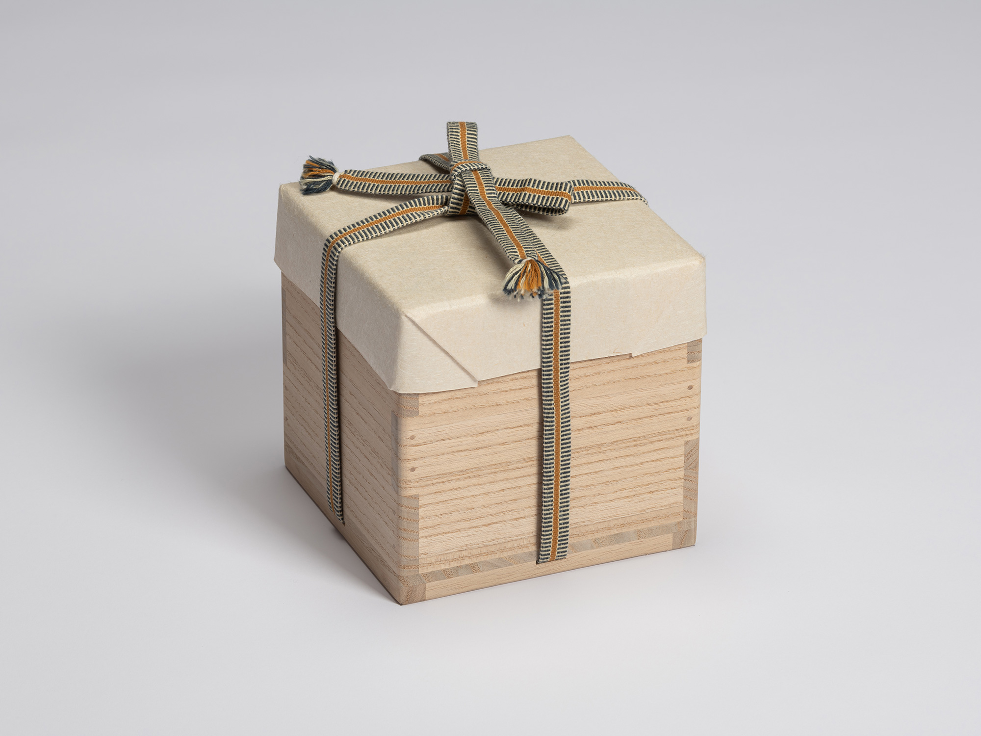 Paulownia wood tomobako wrapped in protective paper and secured with a blue, gray, and ochre striped...
