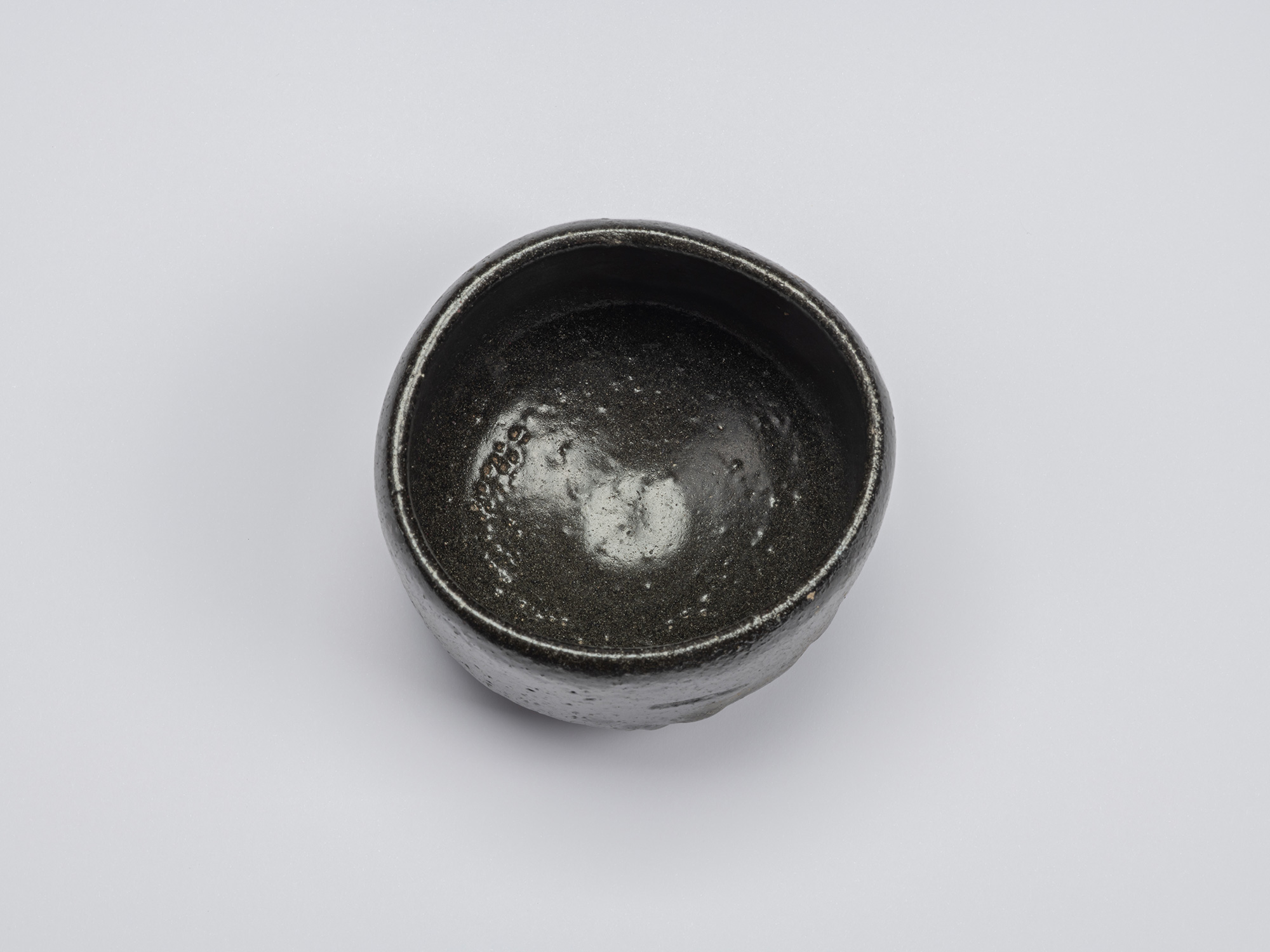 Overhead view of Chawan No. 10 by Shiro Tsujimura, showing a glossy charcoal-black interior with...