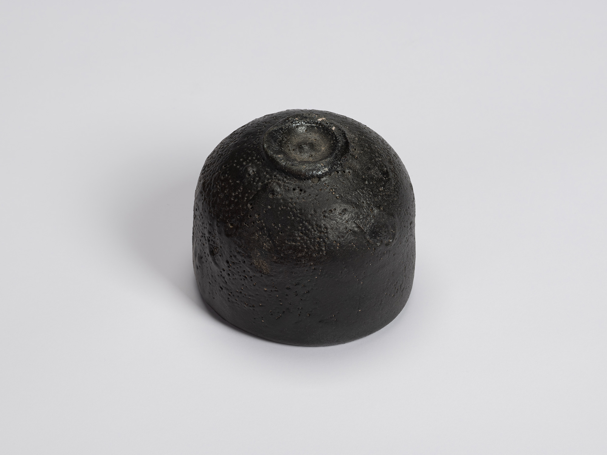 Underside of Chawan No. 11 revealing a small circular foot ring surrounded by a dark, textured...