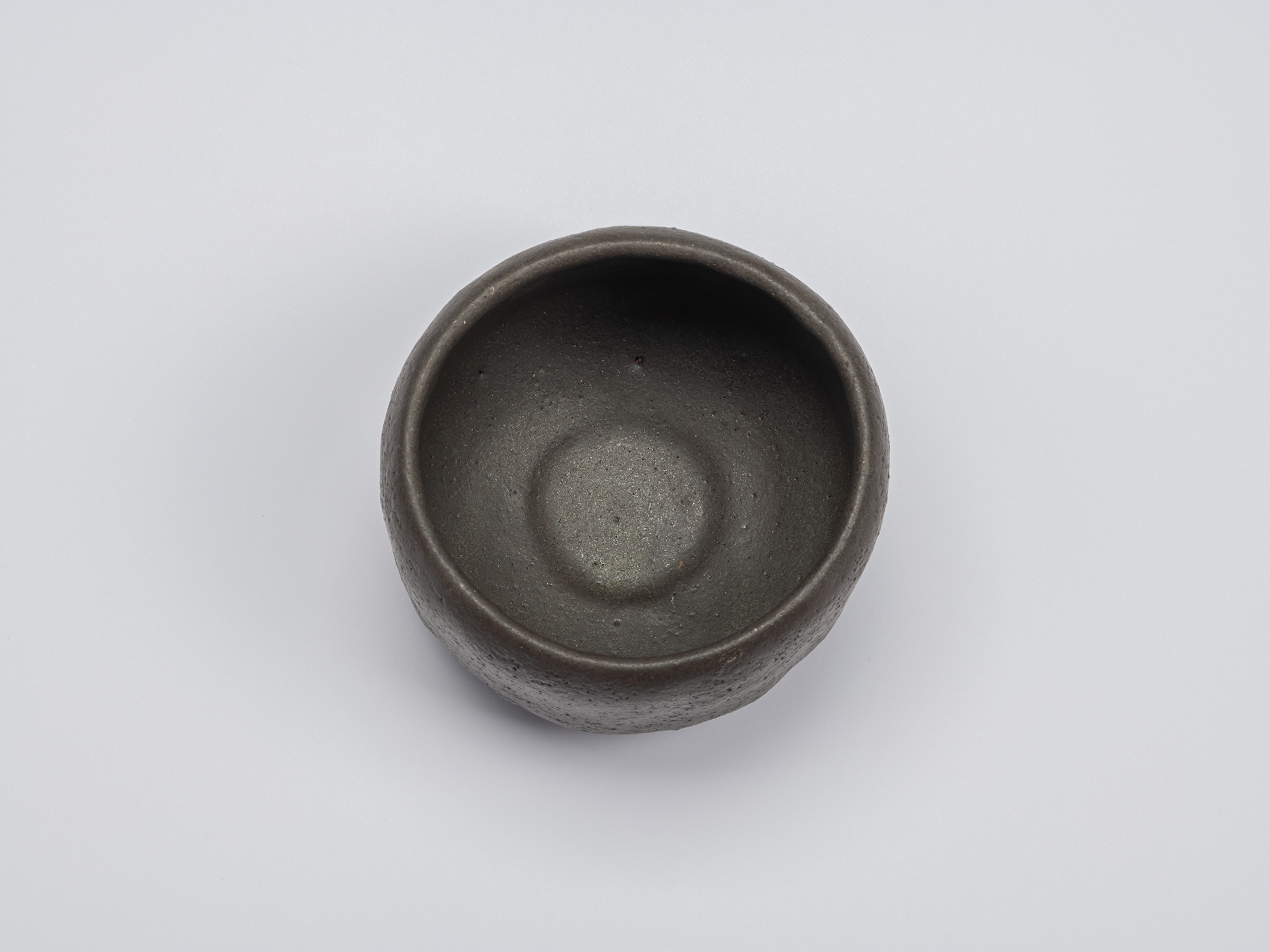 Overhead view of Chawan No. 12 by Shiro Tsujimura showing a matte charcoal-gray interior with a...