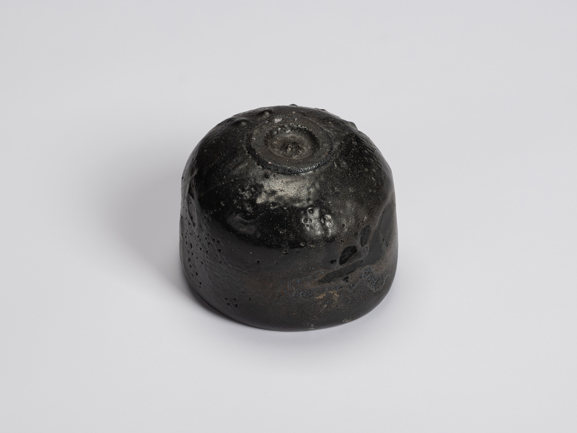 Bottom view of Chawan No. 15 revealing its compact circular foot ring and glossy black exterior...