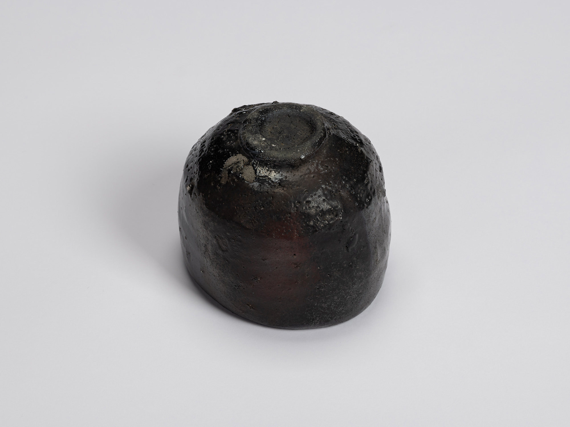 Underside of Kuro Chawan showing its compact carved foot ring and rounded base. Glossy black glaze...