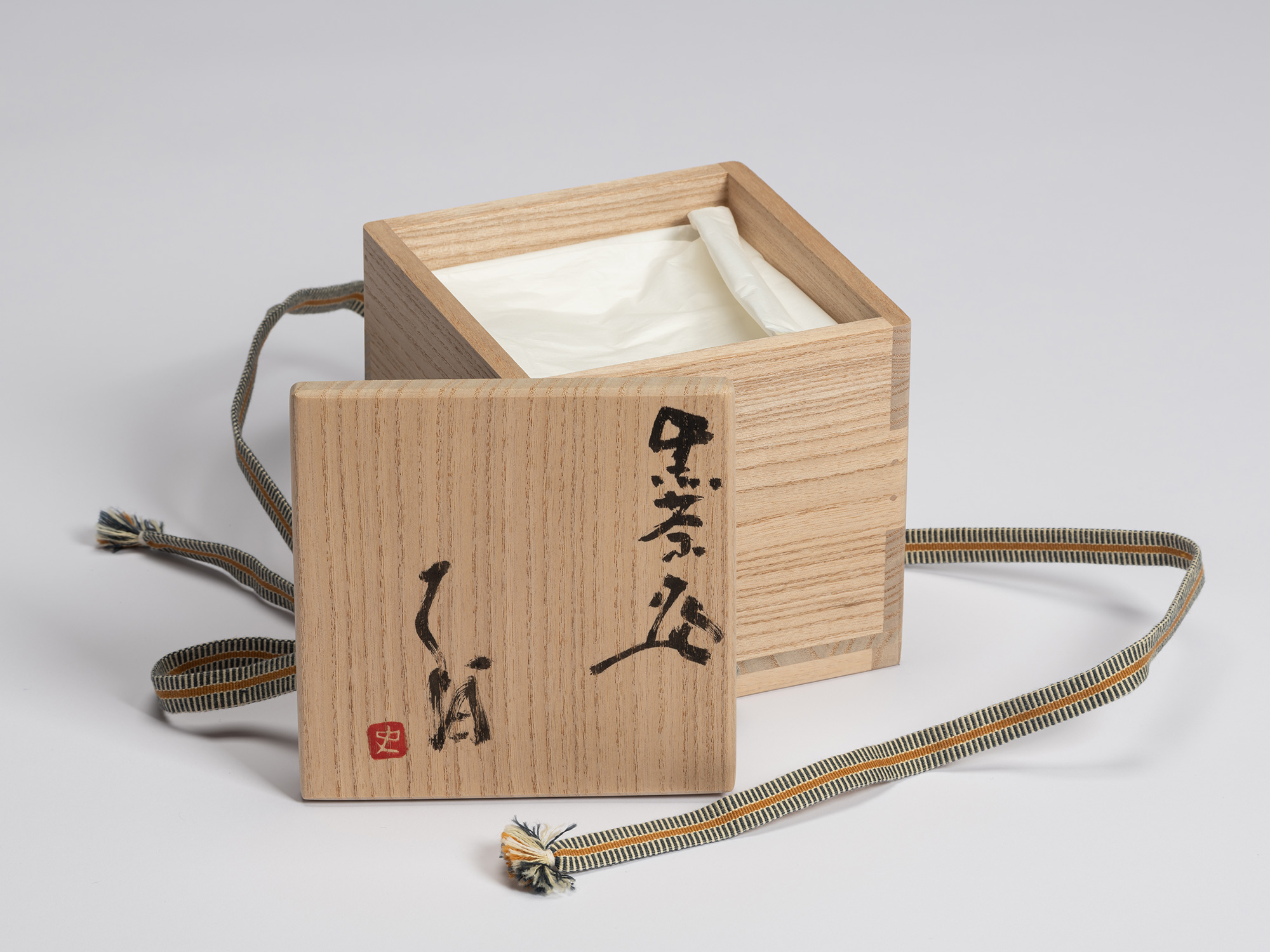 Open paulownia wood tomobako with the lid placed in front of the box. The lid is inscribed in black...