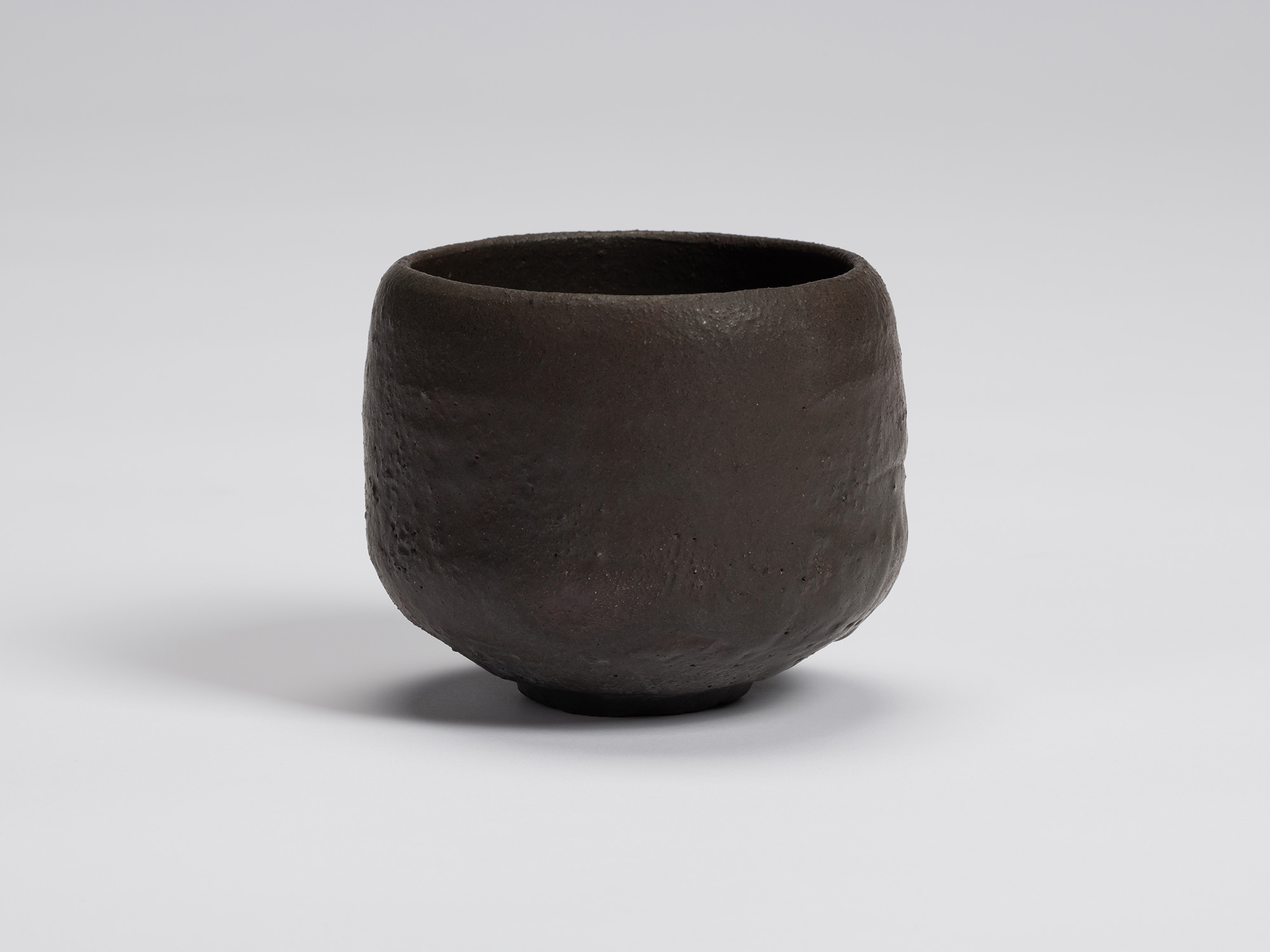 Hand-formed black tea bowl by Shiro Tsujimura with a rounded cylindrical form, gently curved sides,...