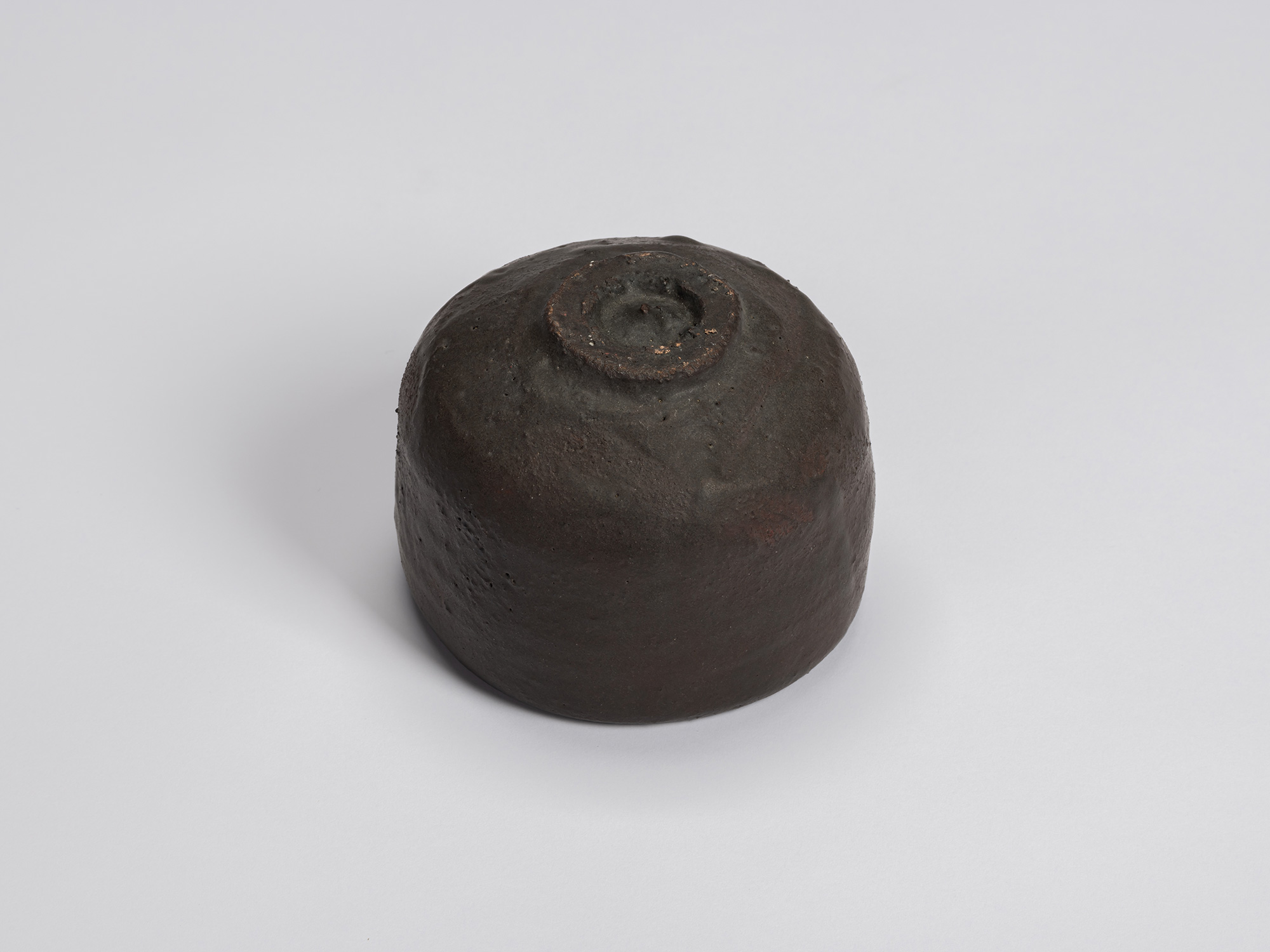 Underside of the black tea bowl showing a small circular foot ring with exposed clay and a rounded...