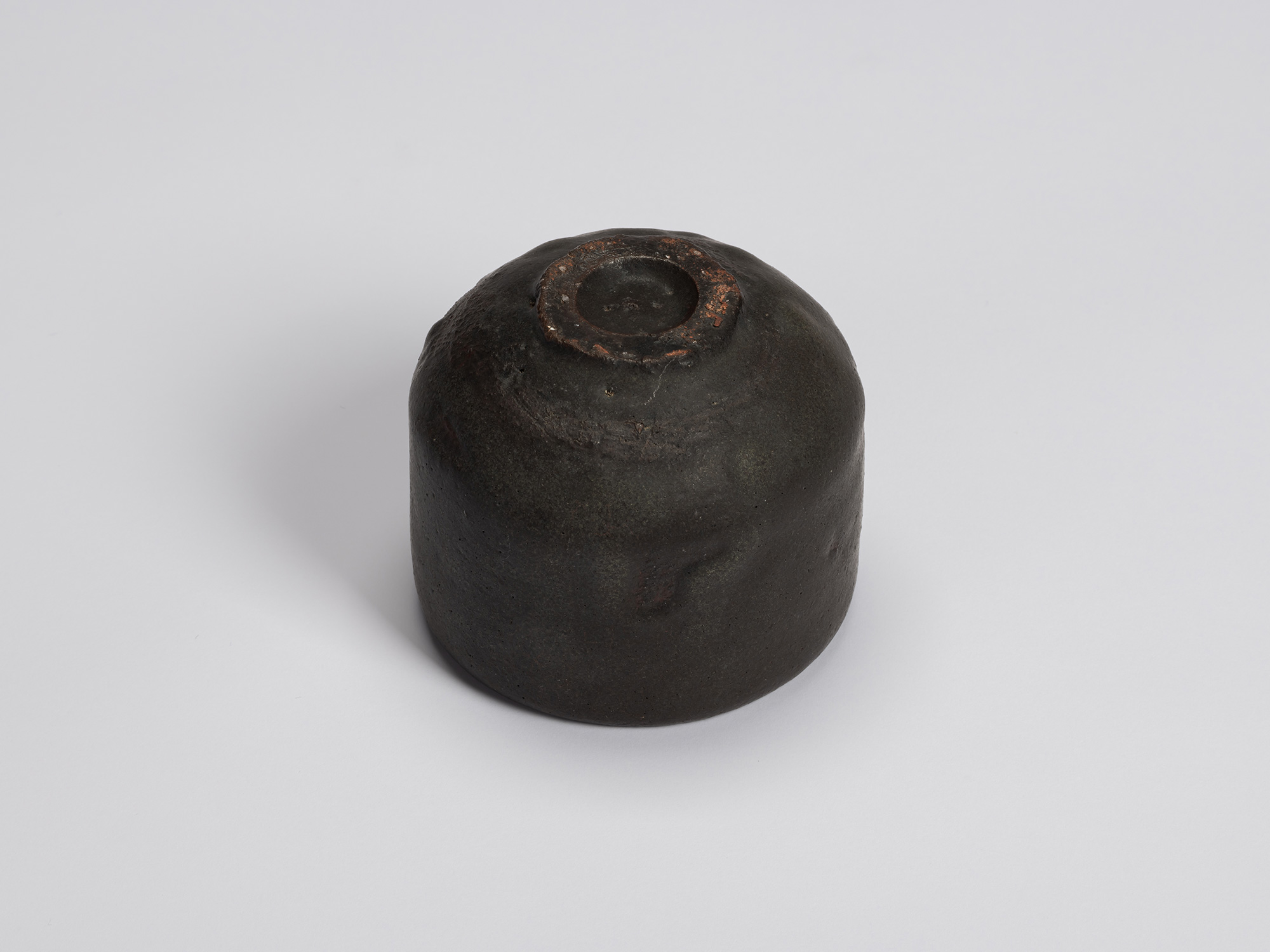 Underside of Kuro Chawan showing its compact carved foot ring and rounded base. The surface transitions...