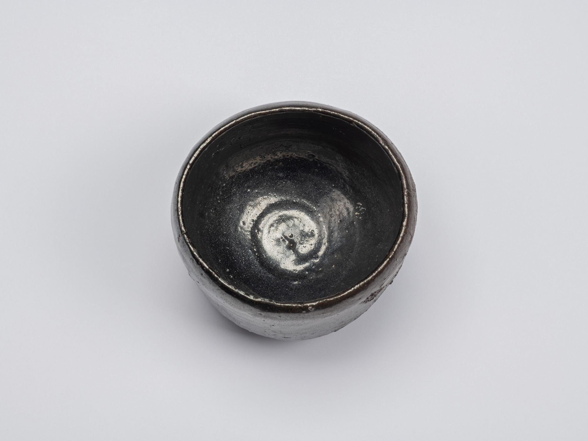Overhead view of the Kuro Chawan showing its irregular circular rim and deep interior, where a...
