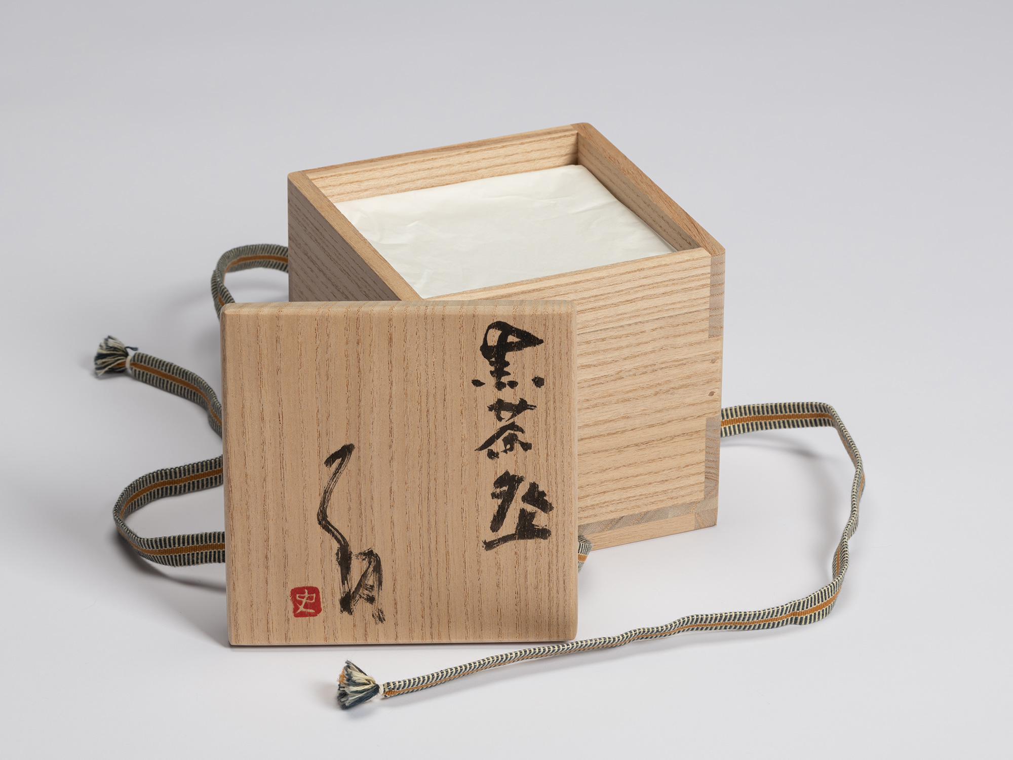 Open kiri wood tomobako for Shiro Tsujimura's Kuro Chawan with the lid placed in front, revealing...