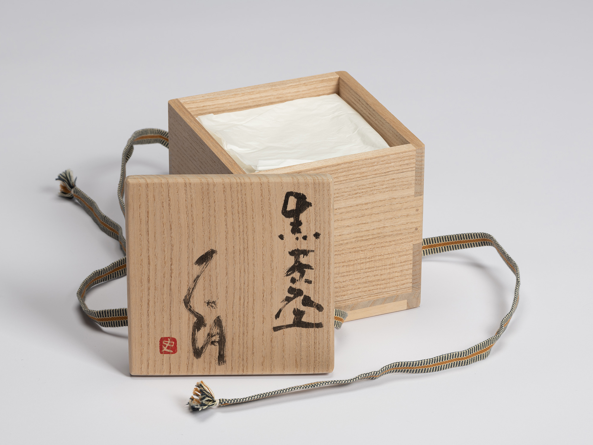 Open paulownia wood tomobako for Shiro Tsujimura's Kuro Chawan with the lid resting beside the...