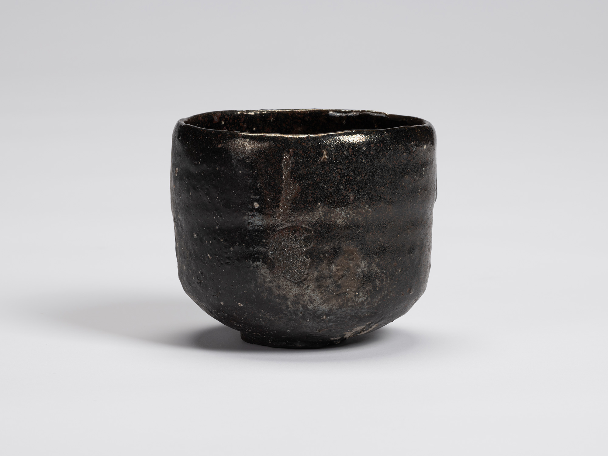 Front view of a hand-formed Kuro Chawan by Shiro Tsujimura featuring a rounded cylindrical form...