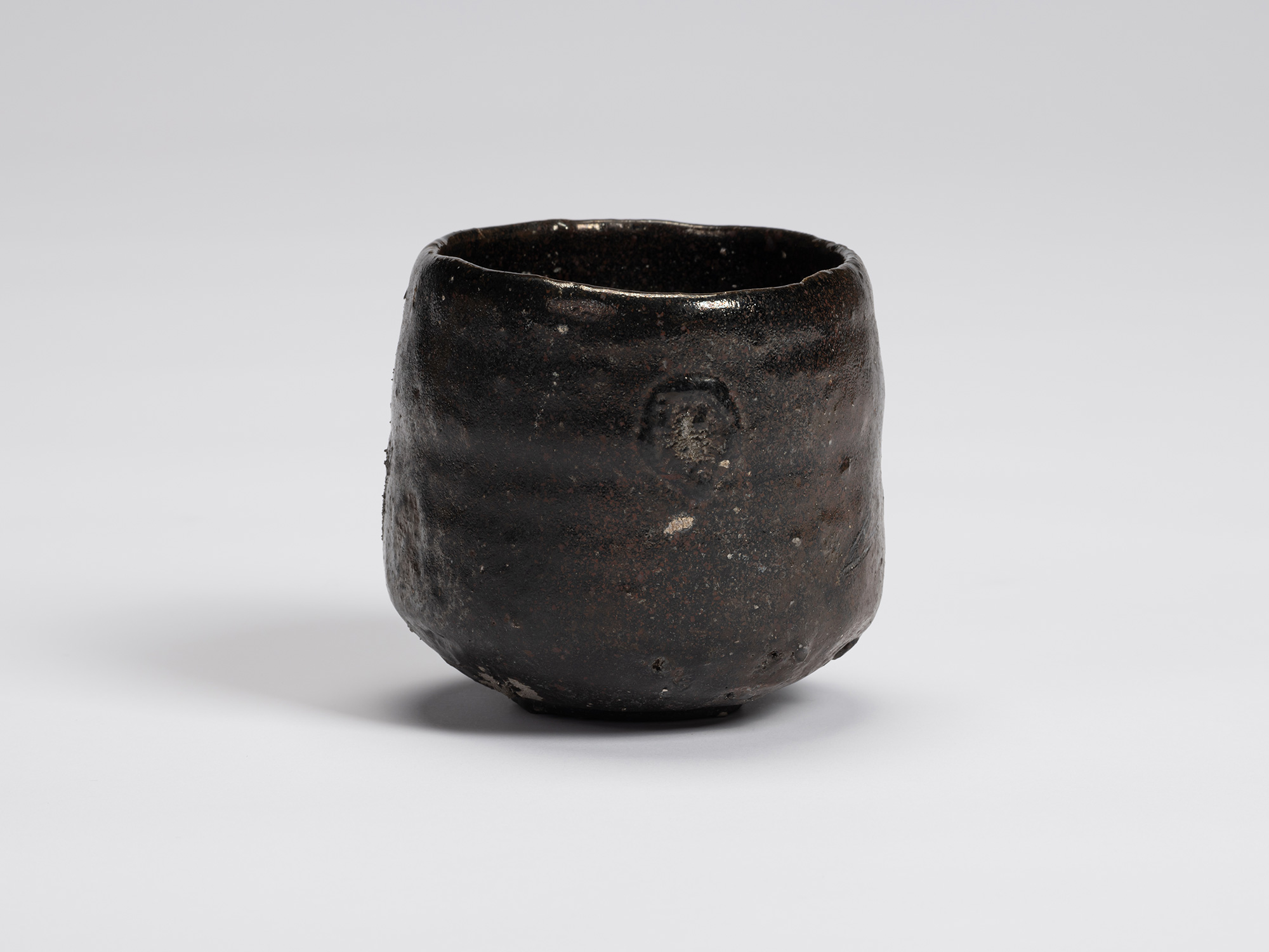 Front view of a hand-formed Kuro Chawan by Shiro Tsujimura featuring a rounded cylindrical form...