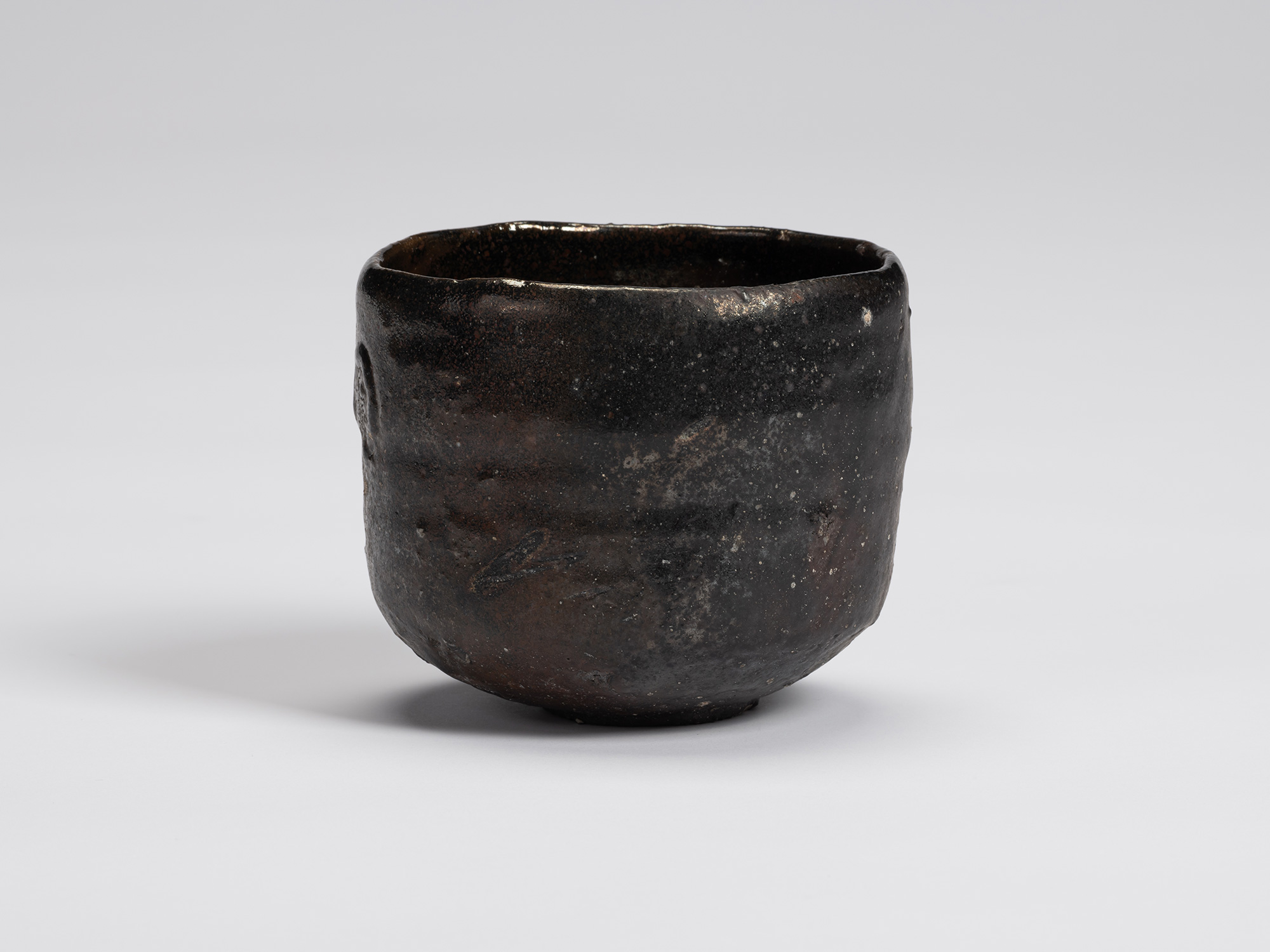 Front view of a hand-formed Kuro Chawan by Shiro Tsujimura featuring a rounded cylindrical form...