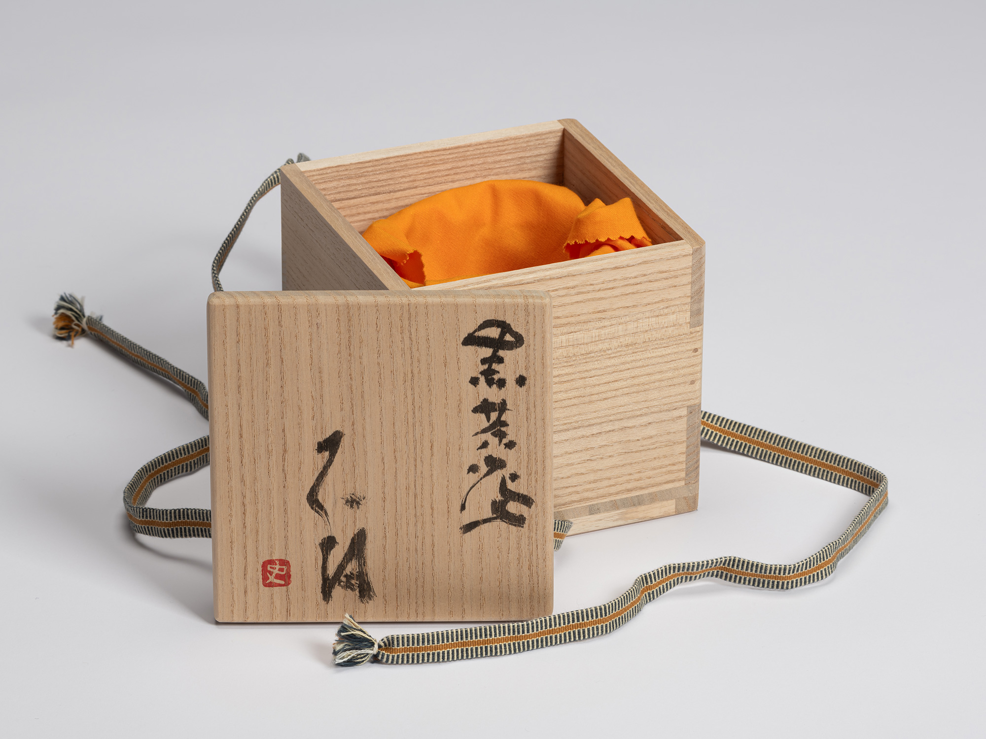 Signed paulownia wood tomobako with the lid removed, revealing the orange protective cloth inside....