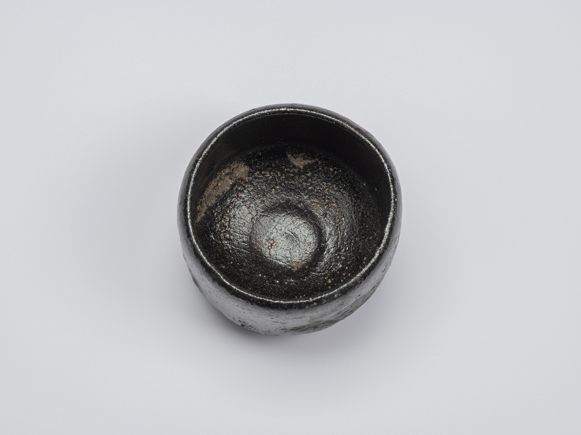 Overhead view of the black-glazed tea bowl showing a deep rounded interior with a glossy dark surface,...