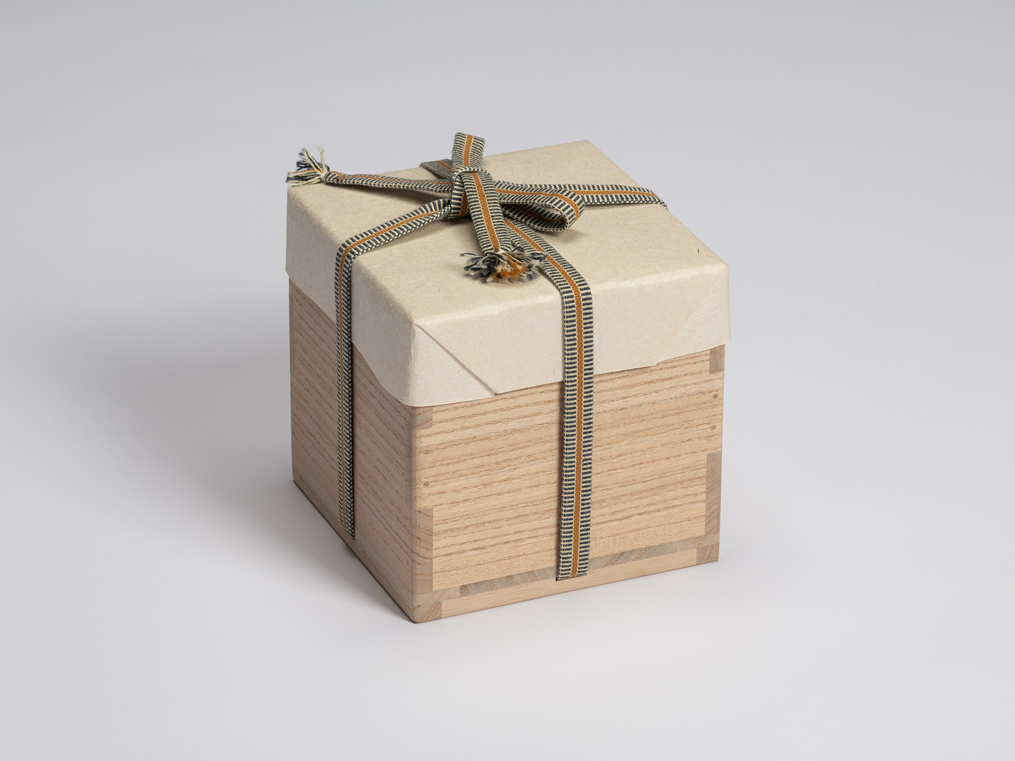 Paulownia wood tomobako wrapped in protective paper and secured with a blue, gray, and ochre striped...