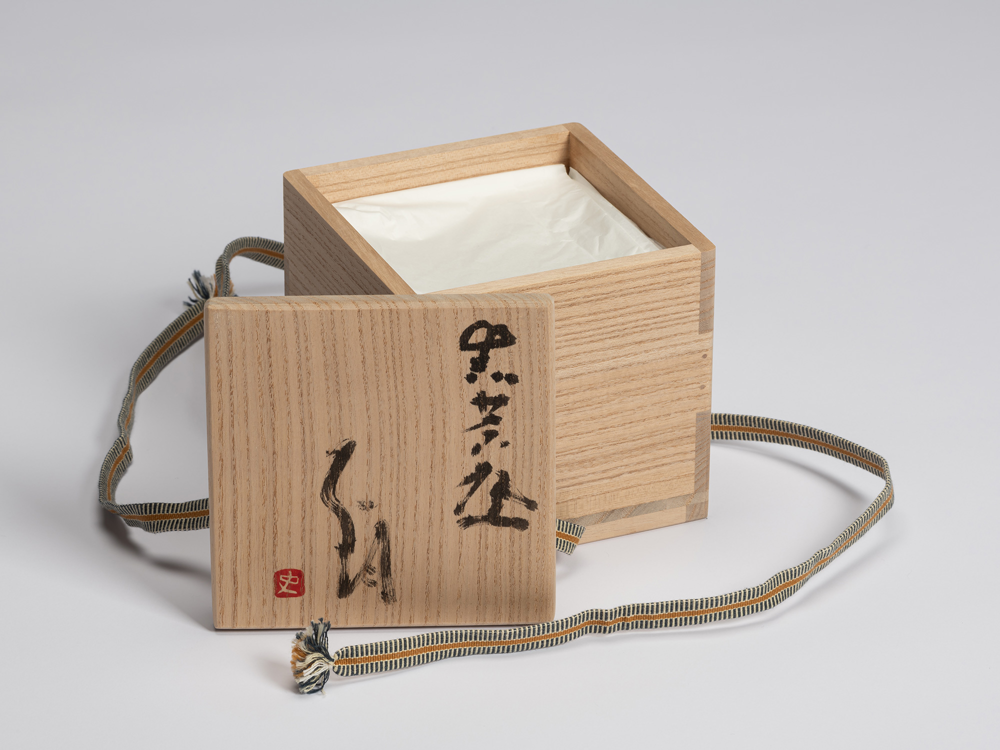 Open paulownia wood tomobako with the lid placed in front of the box. The lid is inscribed in black...