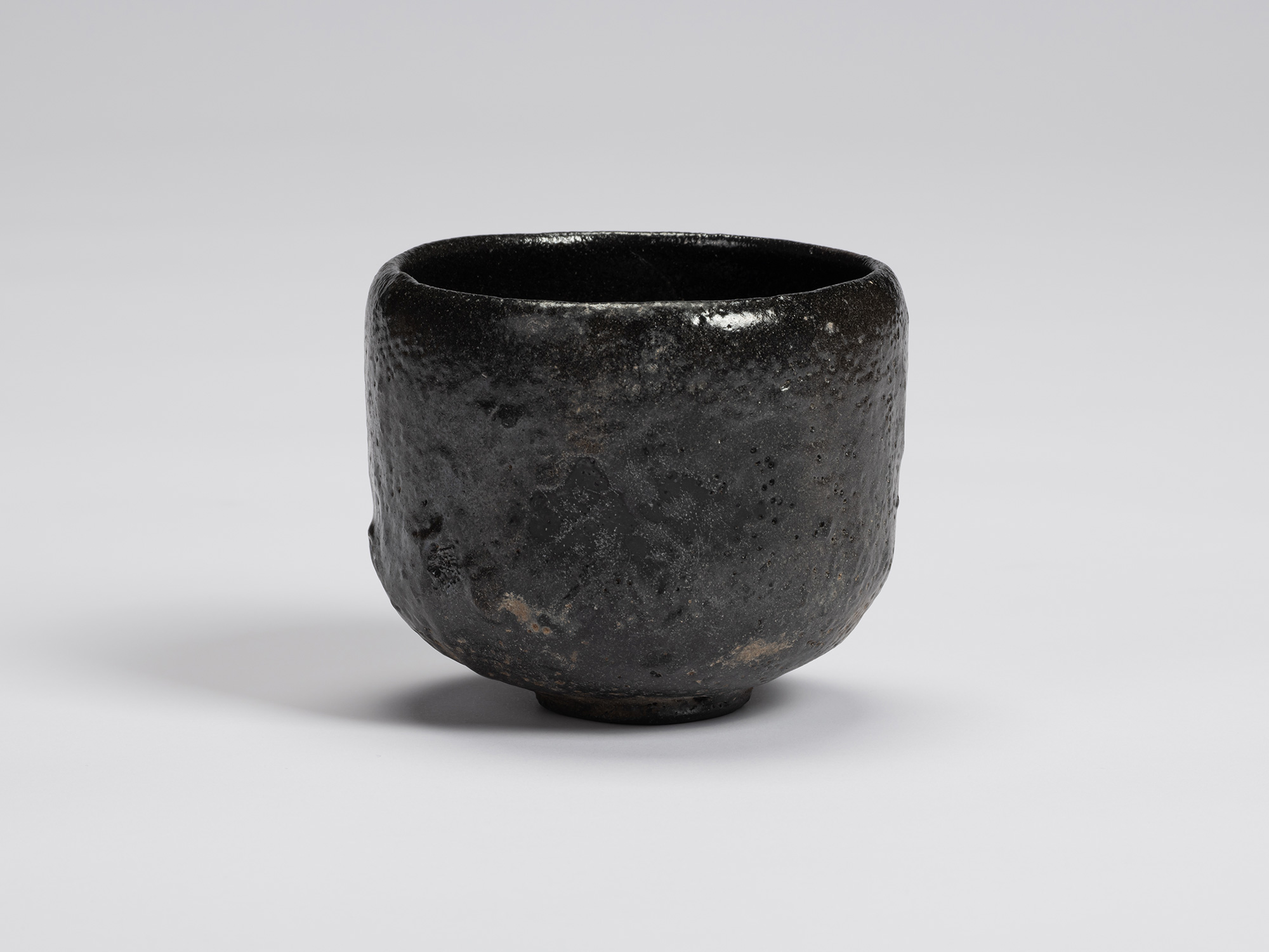 Black-glazed tea bowl by Shiro Tsujimura with a rounded cylindrical form, gently tapered base,...