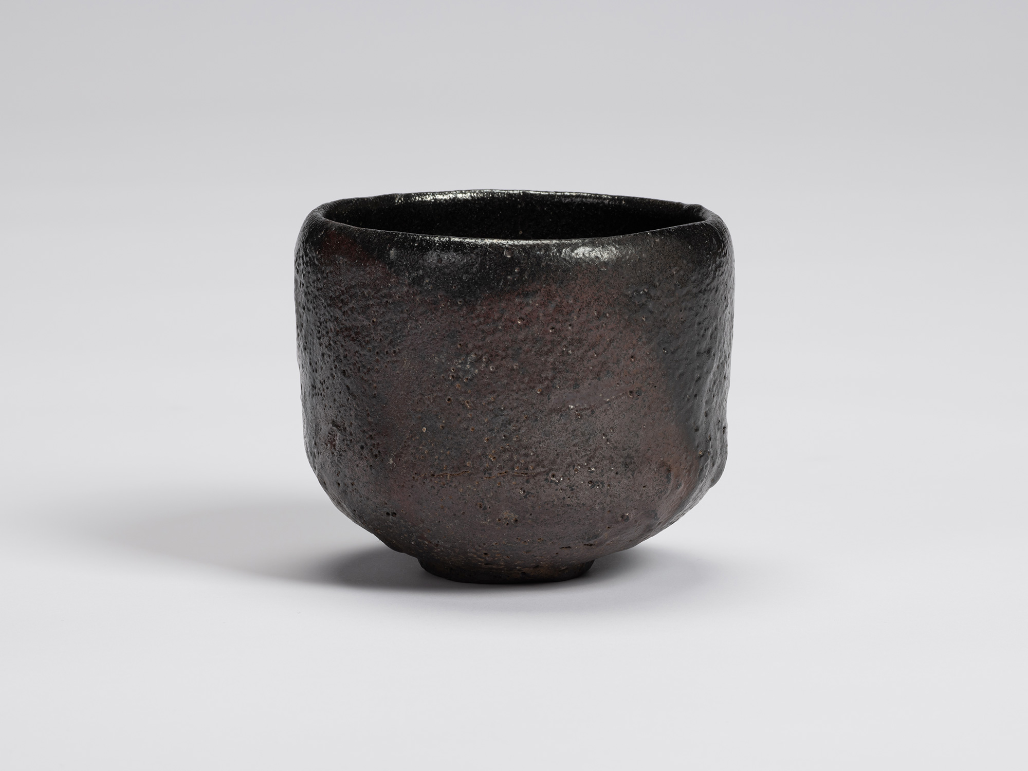 Black-glazed tea bowl by Shiro Tsujimura with a rounded cylindrical form, gently tapered base,...