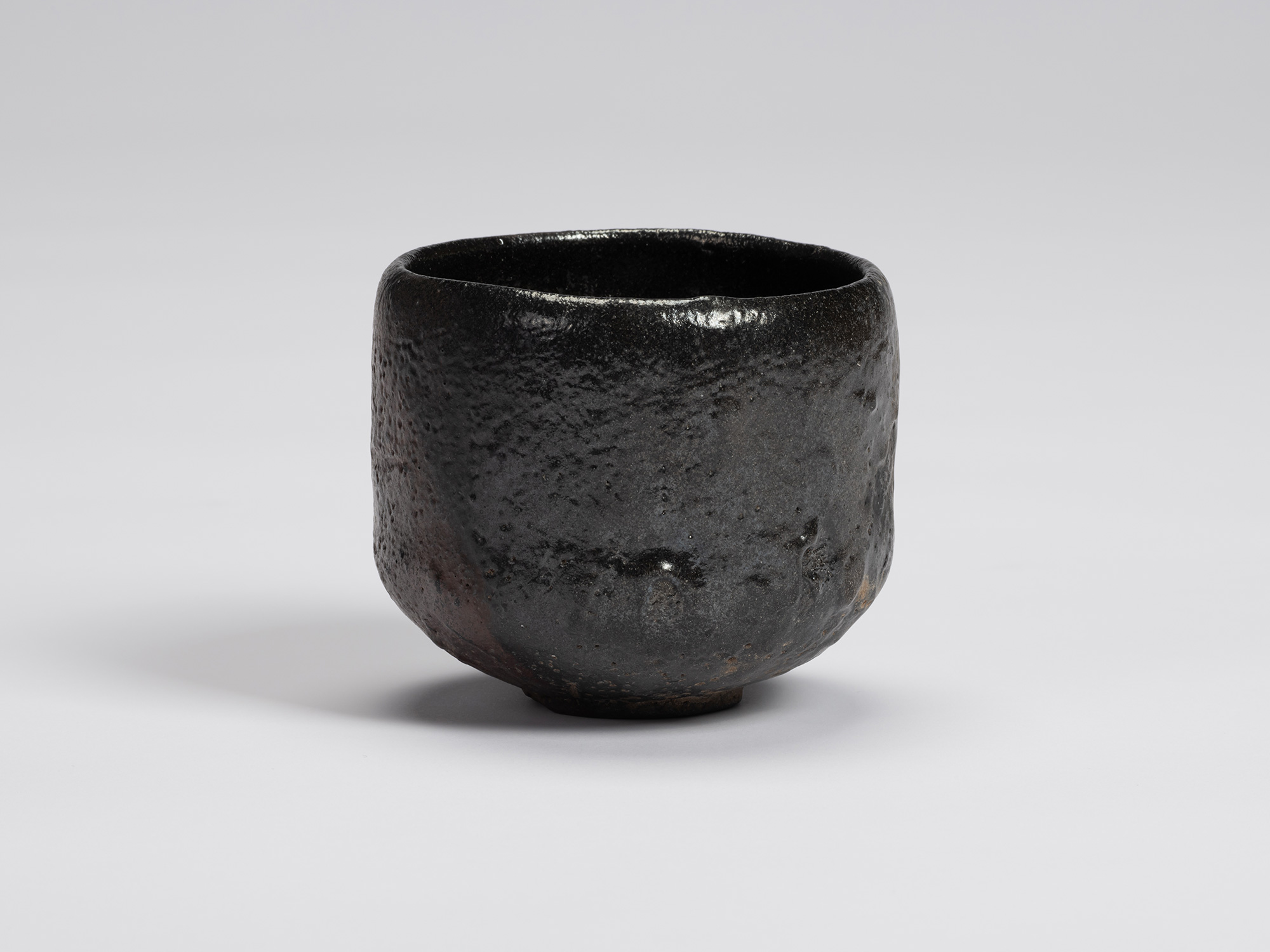 Black-glazed tea bowl by Shiro Tsujimura with a rounded cylindrical form, gently tapered base,...