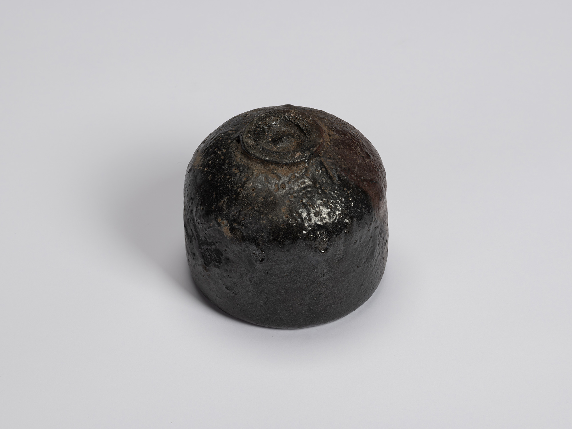 Underside of the black-glazed tea bowl showing a small circular foot ring surrounded by a rounded...