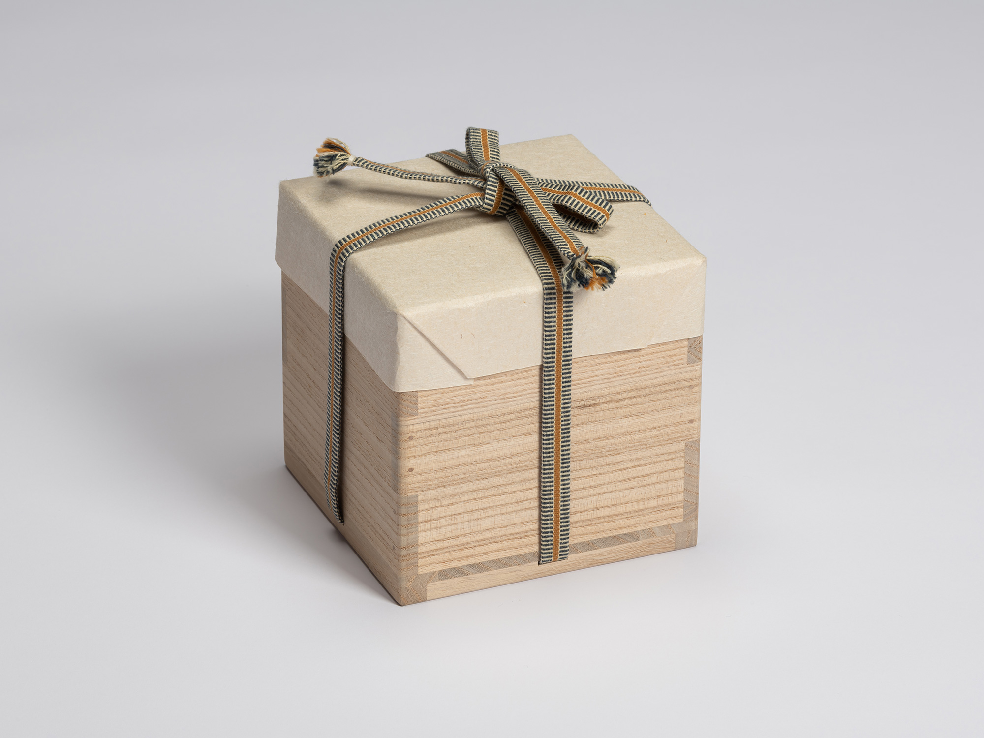 Paulownia wood tomobako wrapped in protective paper and secured with a blue, gray, and ochre striped...