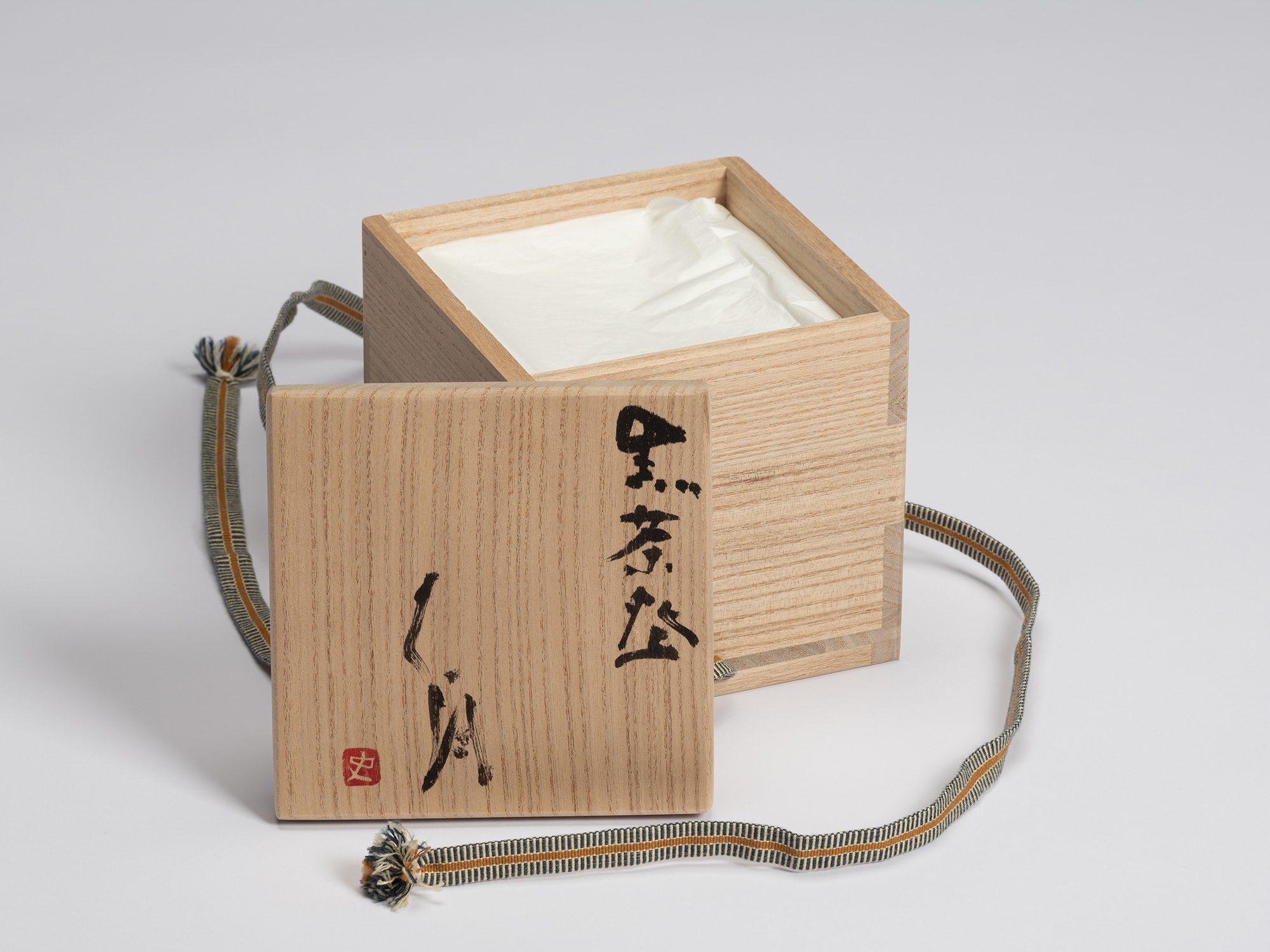 Open paulownia wood tomobako with the lid placed in front of the box. The lid is inscribed in black...