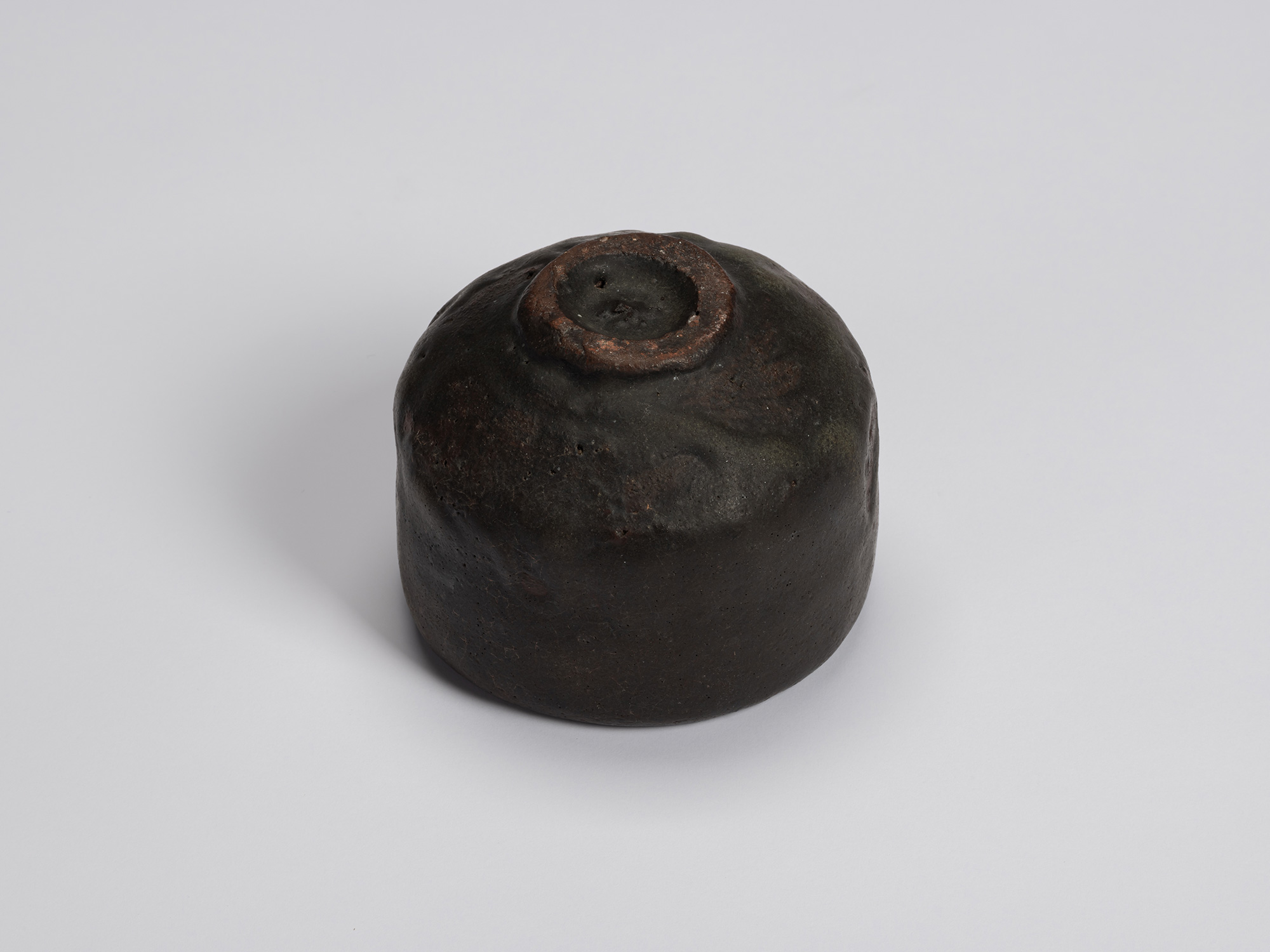 Underside of the black tea bowl showing a small circular foot ring with exposed clay and a rounded...