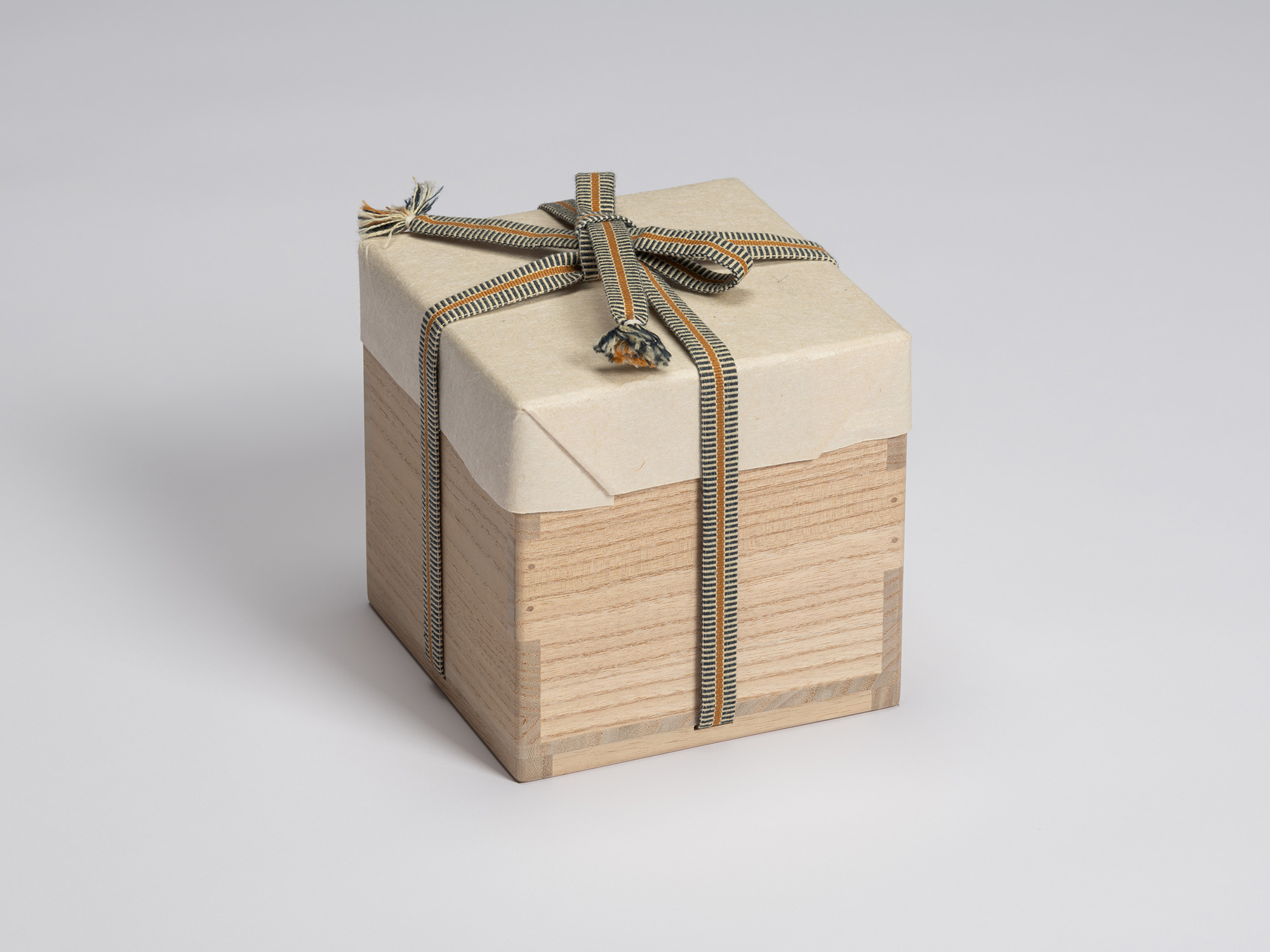 Paulownia wood tomobako wrapped in protective paper and secured with a blue, gray, and ochre striped...