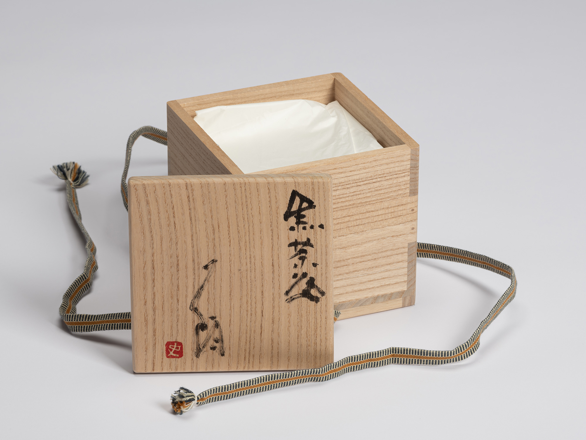 Open paulownia wood tomobako with the lid placed in front of the box. The lid is inscribed in black...