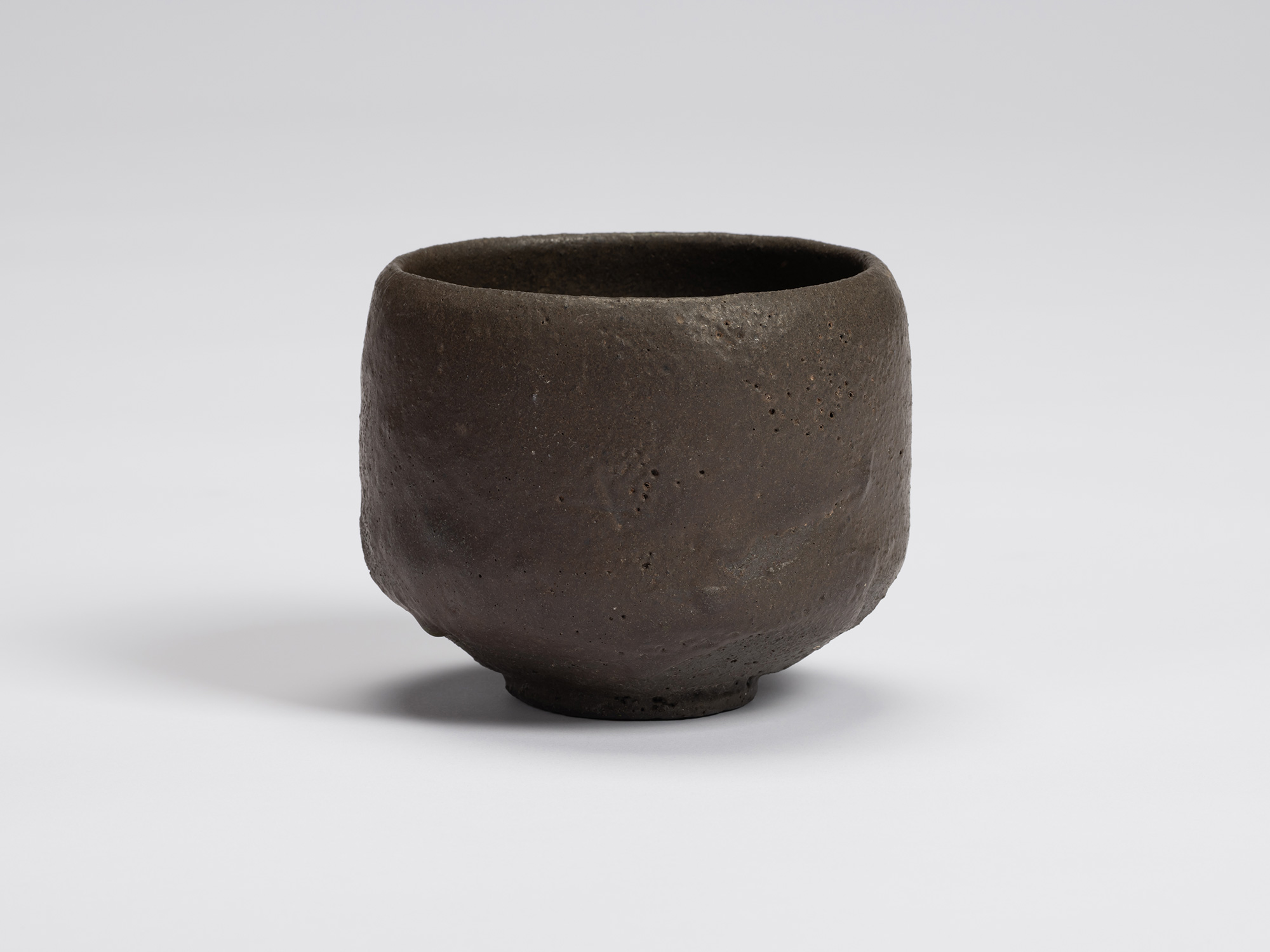 Hand-formed black tea bowl by Shiro Tsujimura with a rounded cylindrical form, gently tapered base,...