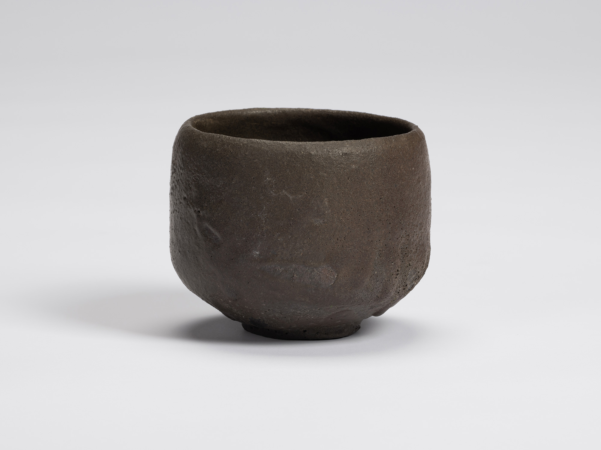 Hand-formed black tea bowl by Shiro Tsujimura with a rounded cylindrical form, gently tapered base,...
