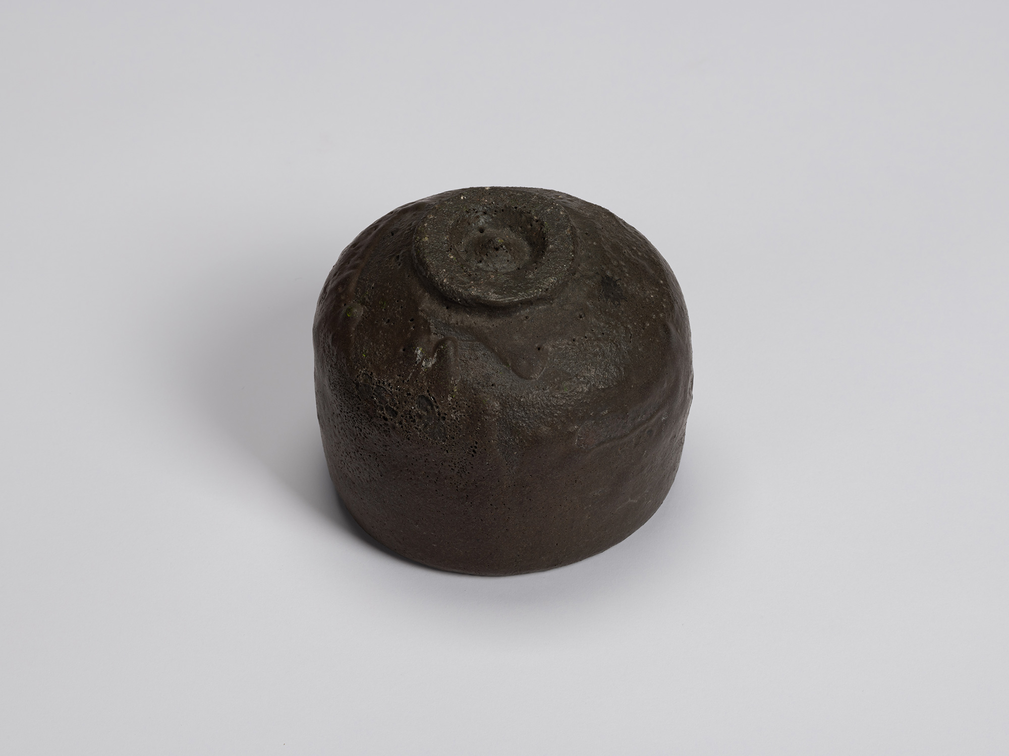 Underside of the black tea bowl showing a small circular foot ring with exposed clay and a rounded...
