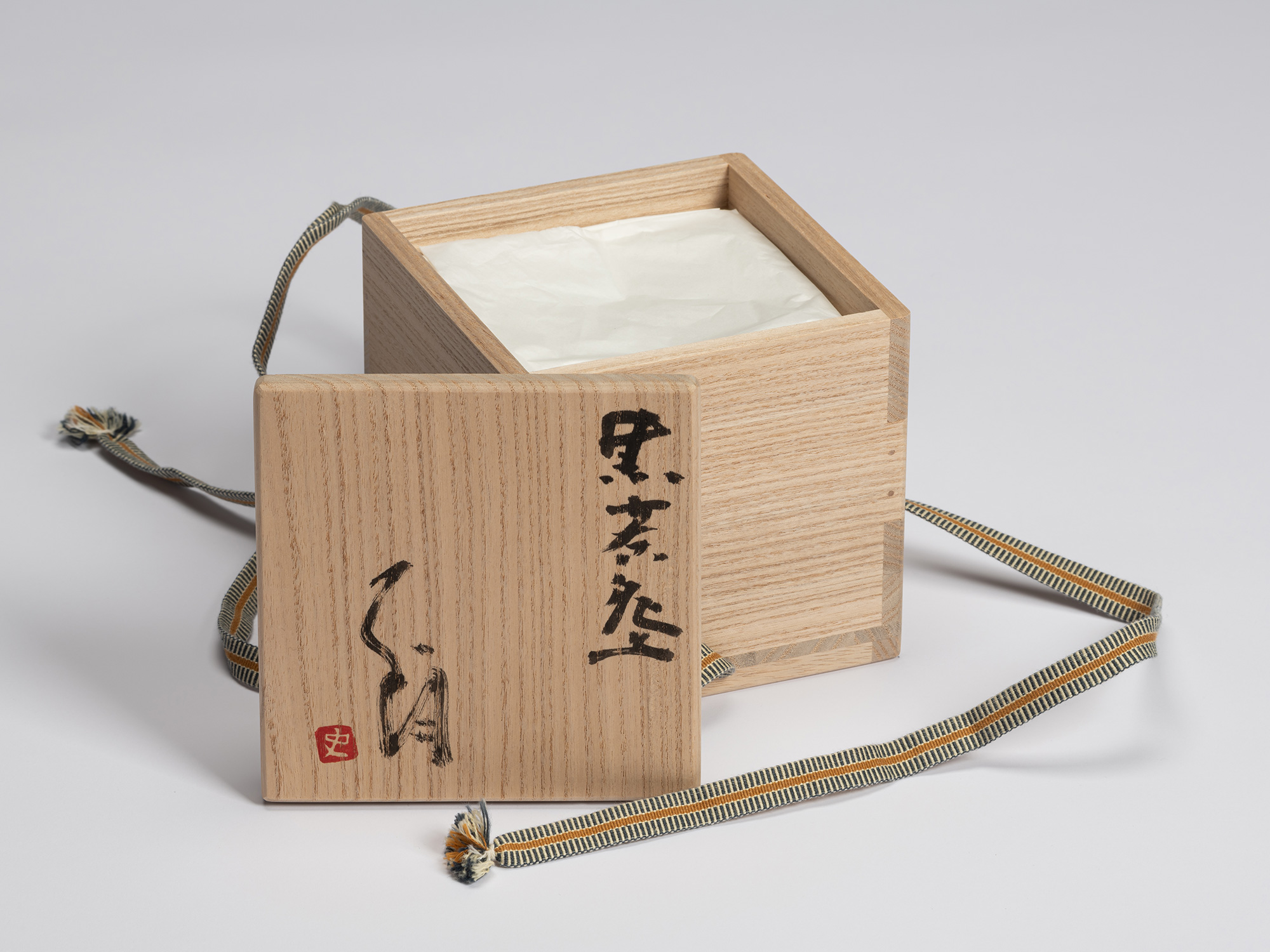 Signed wooden tomobako displayed with the lid removed beside the paulownia storage box lined with...