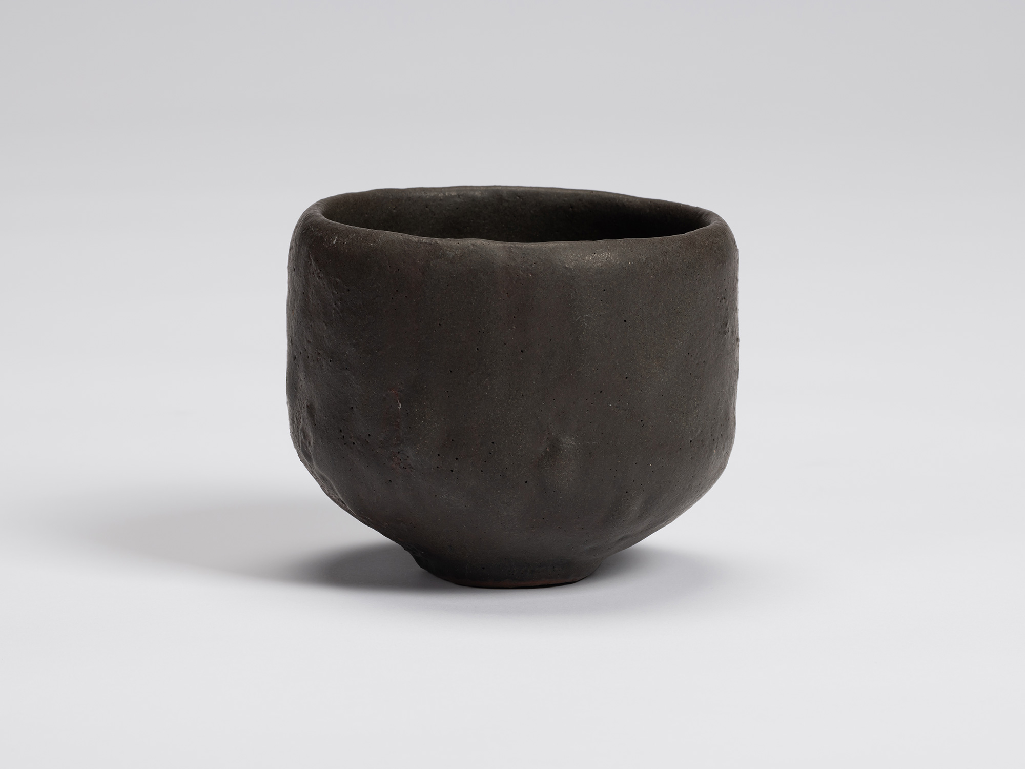 Front view of Shiro Tsujimura's hand-formed black tea bowl with a rounded cylindrical form, matte...