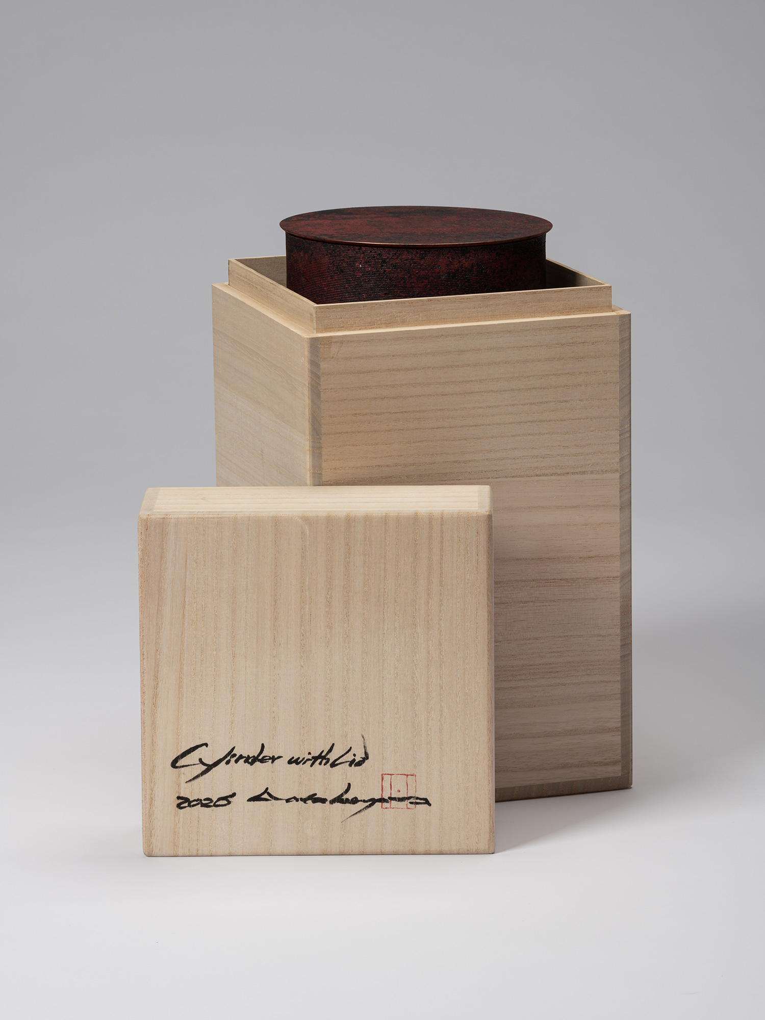 Open tomobako for Cylinder with Lid - Red. Box lid is removed and top of cylinder is visible protruding...